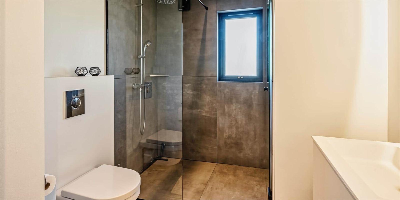 Badezimmer mit Dusche, Toilette und Waschtisch. Fenster mit blauem Rahmen.