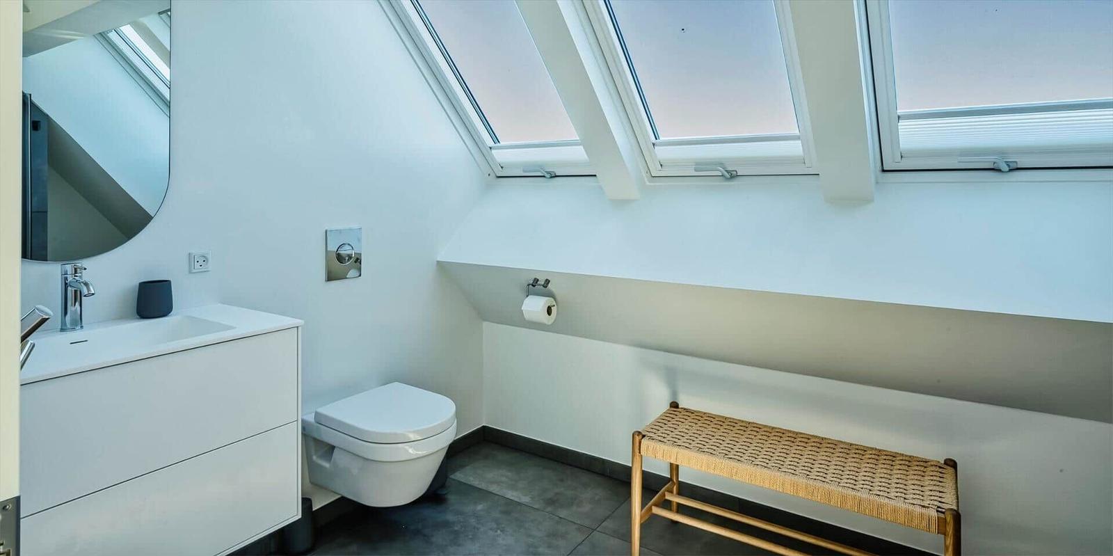 Badezimmer mit Dachfenstern, Waschbecken, Toilette und Bänkchen.