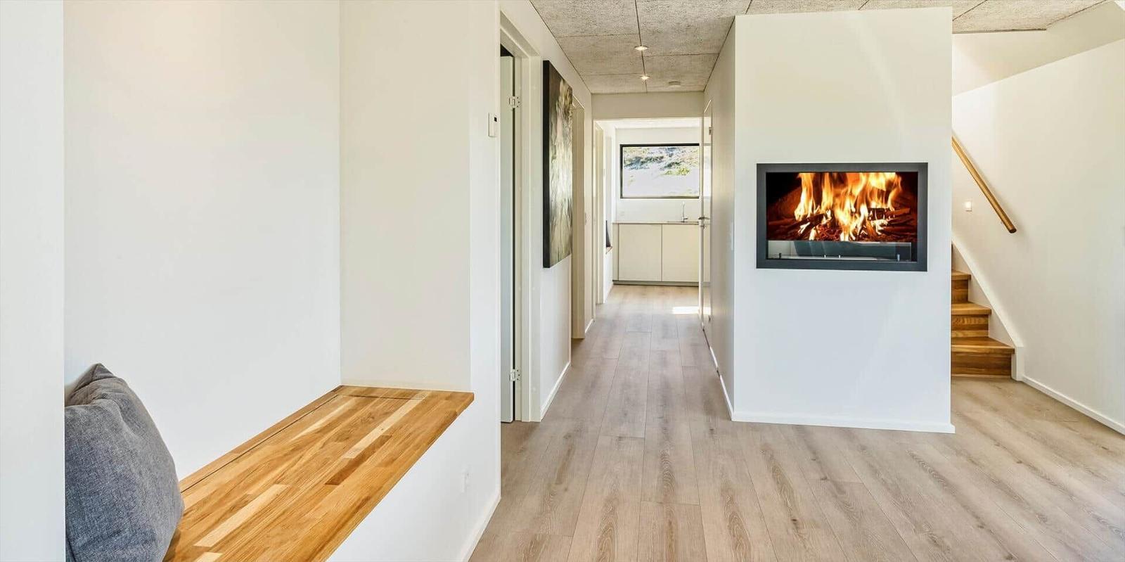 Hallenraum mit integriertem Kamin und Holzboden. Links Sitzbank, rechts Treppe.