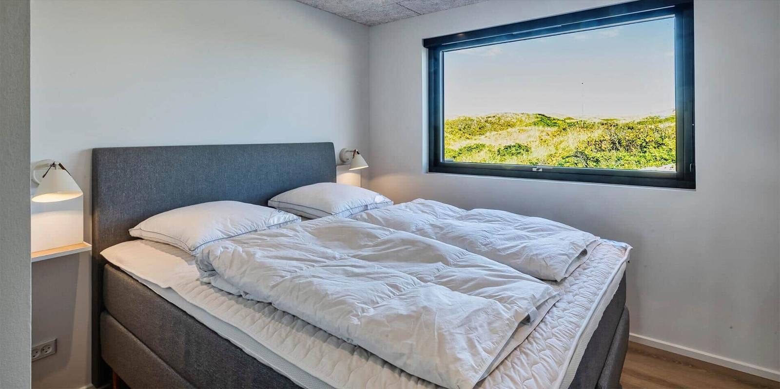 Schlafzimmer mit Doppelbett und großem Fenster zur Landschaft.
