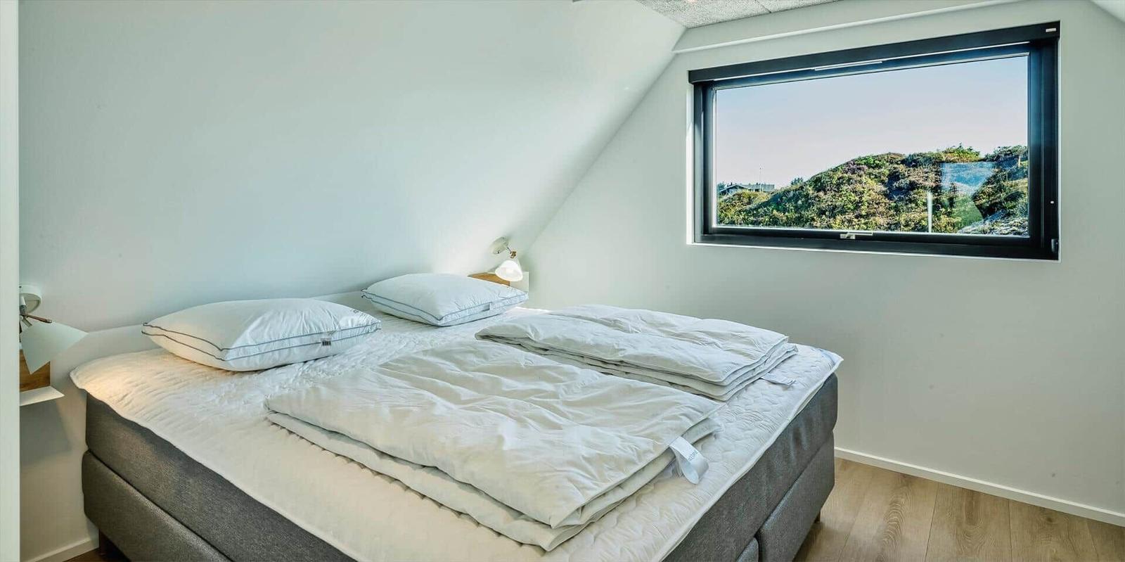 Schlafzimmer mit Doppelbett und großem Fenster mit Blick auf die Landschaft.