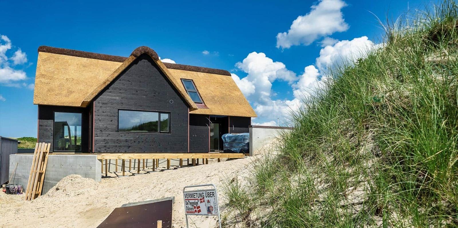 Moderne Strandhaus mit Strohdach und Holzterrasse auf Sanddüne