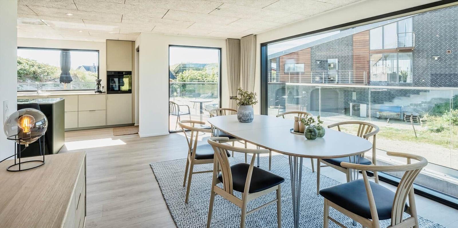 Esszimmer mit Tisch und Stühlen, große Fenster und Blick auf Außenbereich.