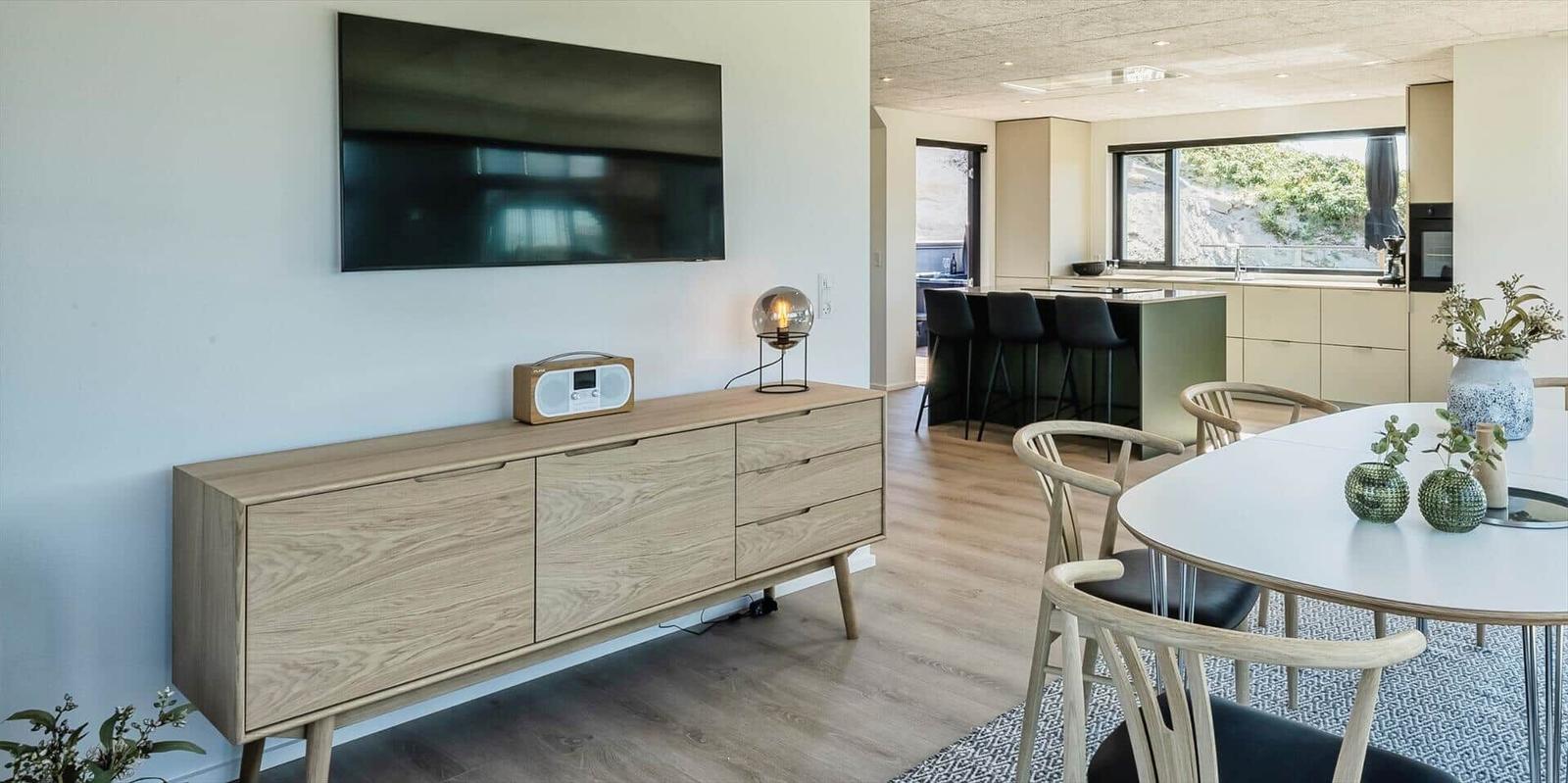 Wohn- und Essbereich mit TV, Sideboard und Esstisch. Küchenbereich im Hintergrund.