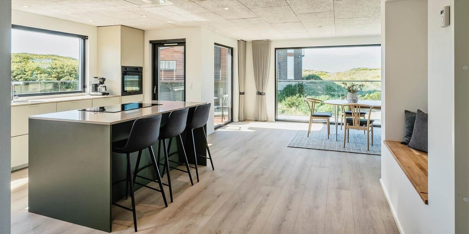 Moderne Küche mit Kücheninsel und Sitzgelegenheiten. Blick auf Balkon und Grünflächen.
