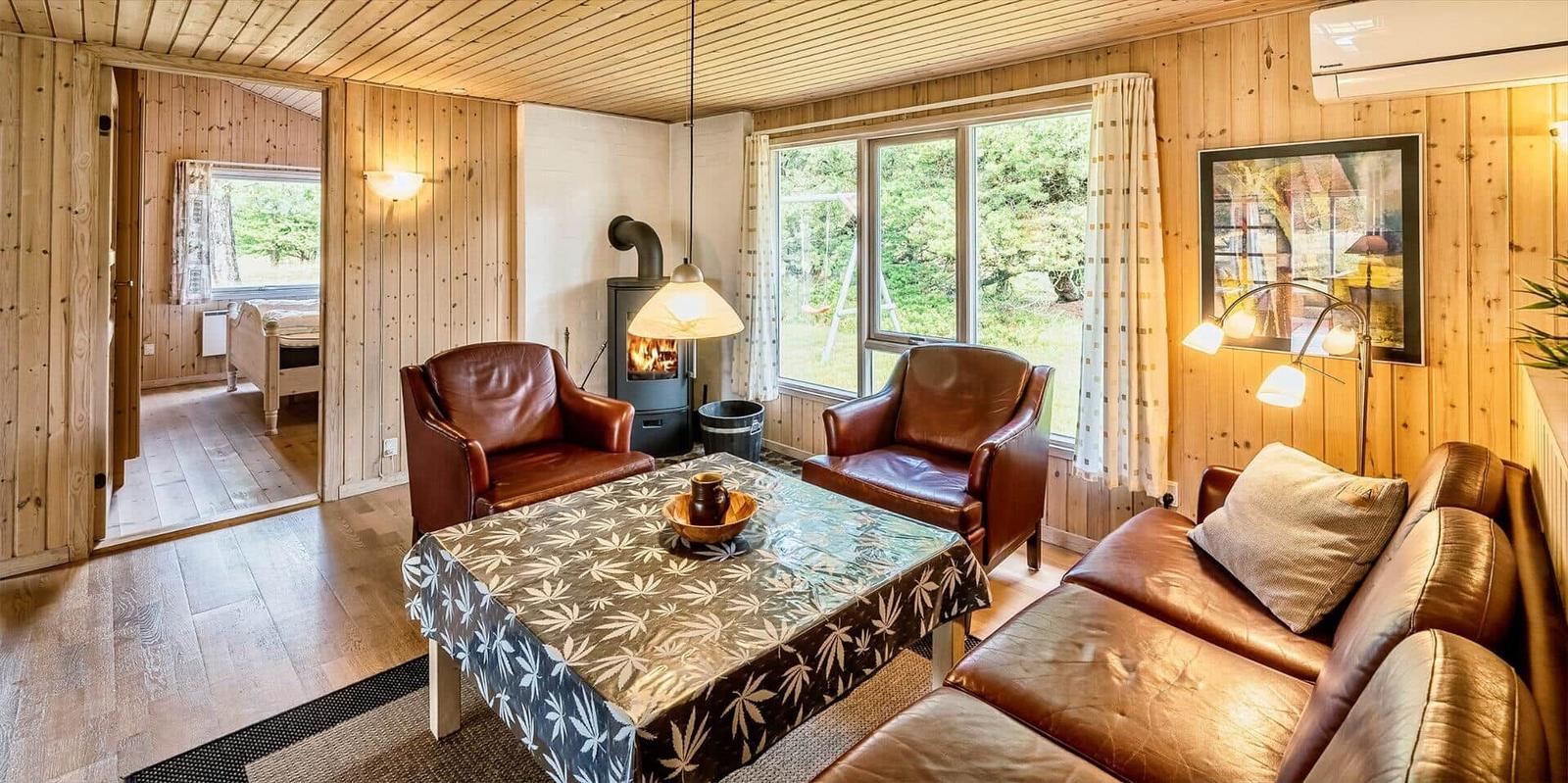 Wohnzimmer mit Holzwand, Sofa, zwei Sesseln und Kamin. Durchgang zur Schlafzimmer.