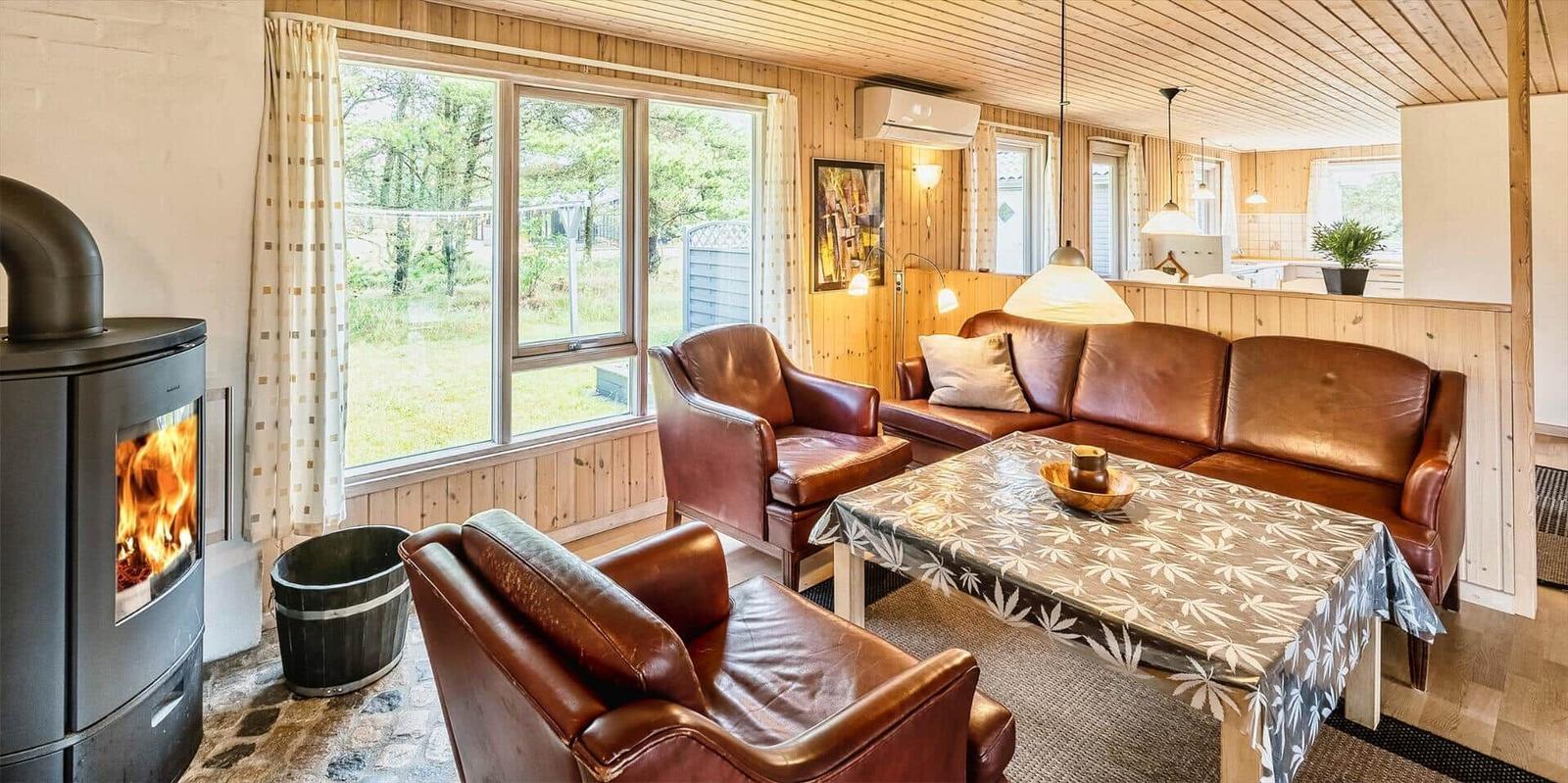 Wohnzimmer mit Holzwänden, Ledersofa, Kamin und großem Fenster.