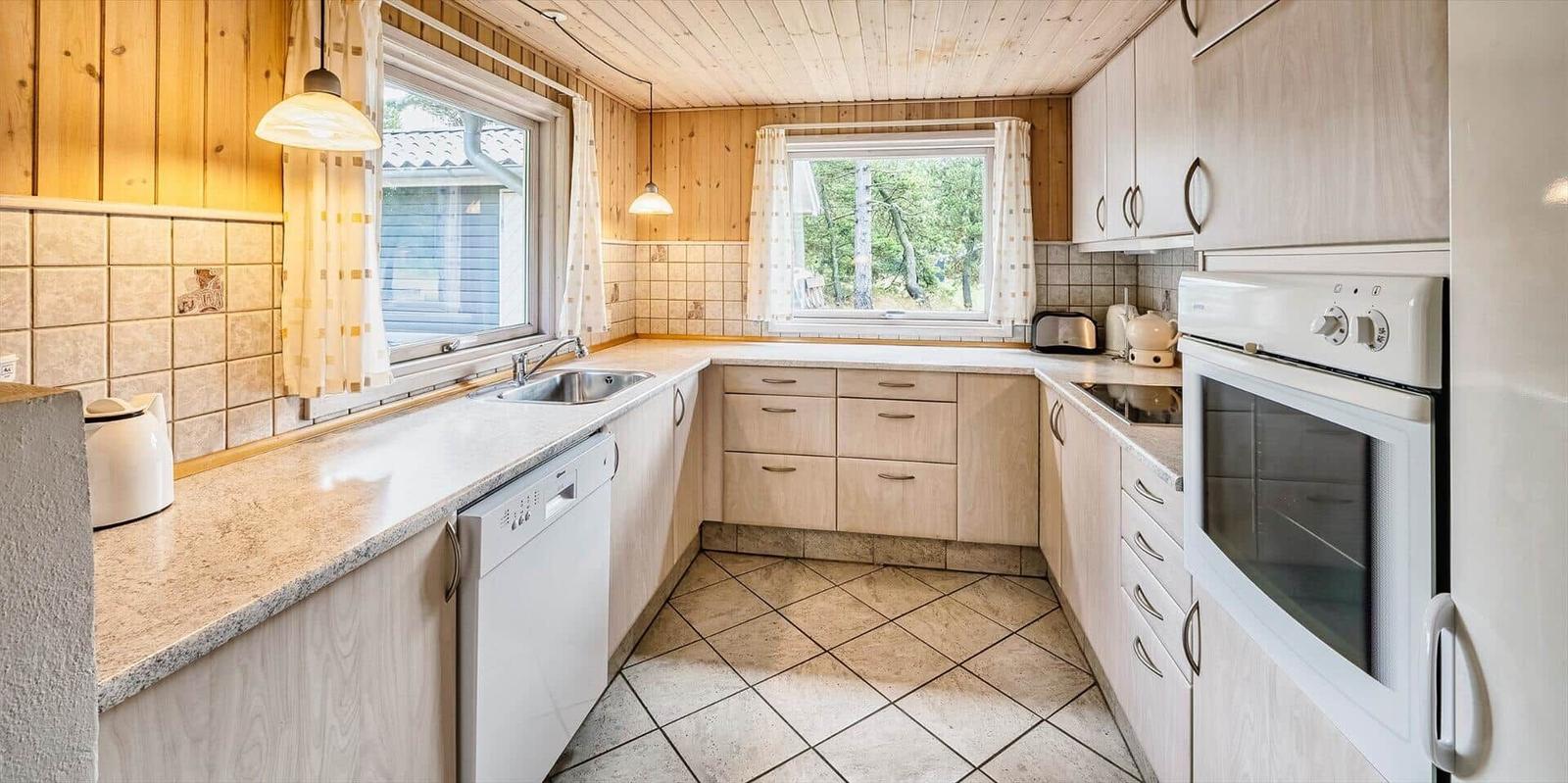 Küche mit Holzwänden, Fenstern und weißen Geräten.
