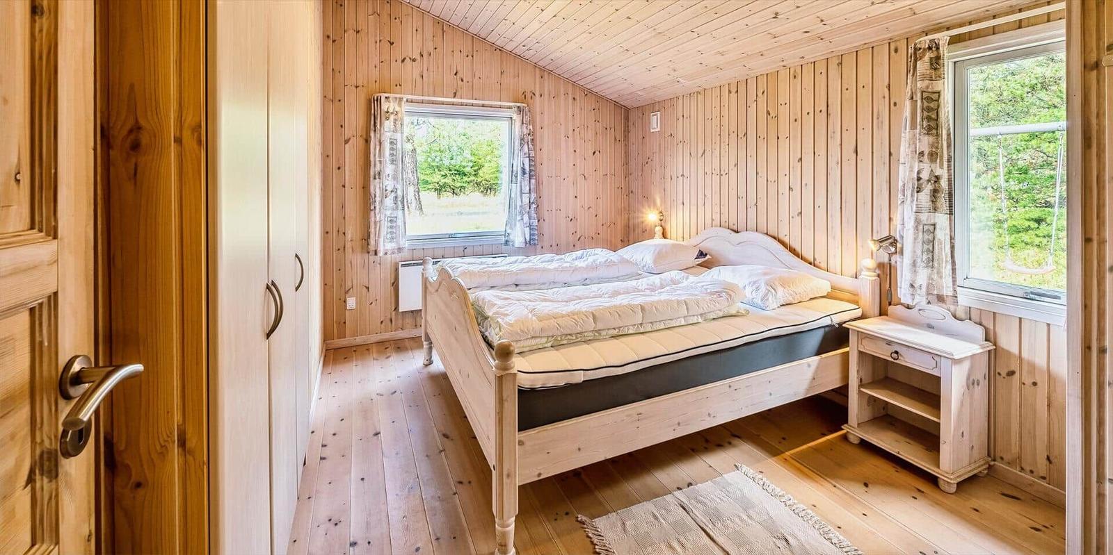 Schlafzimmer mit Holzwandverkleidung, Bett, Nachttisch und Fenstern.