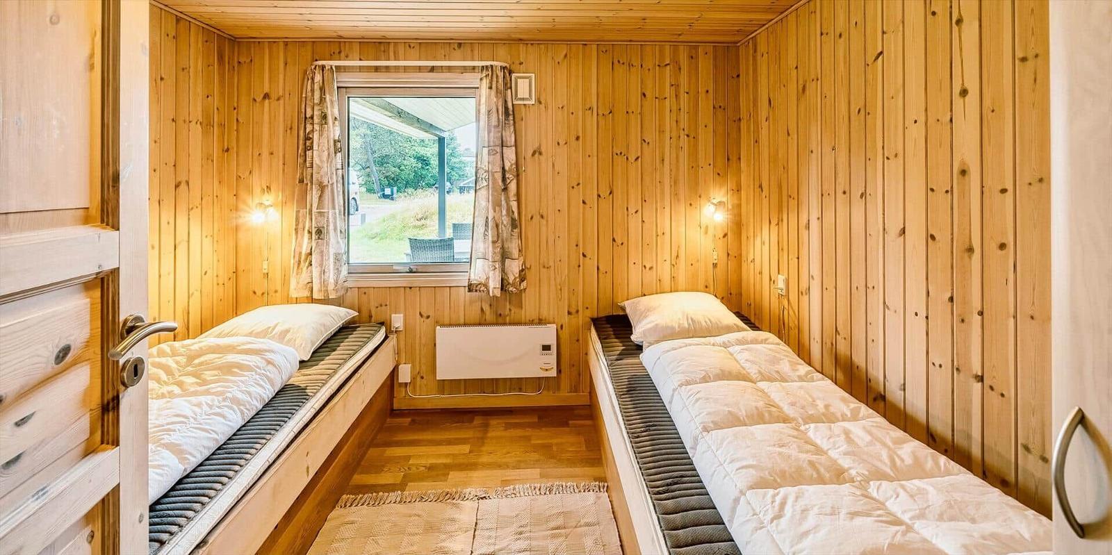Zwei Einzelbetten in einem Holzraum mit Fenster und Heizung.