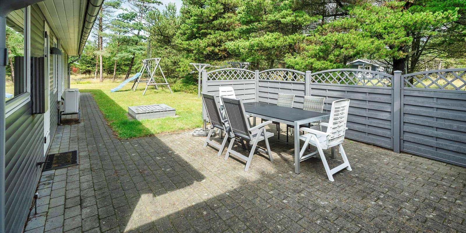 Terrasse mit Tisch und Stühlen, umgeben von einem Zaun und Grünfläche.