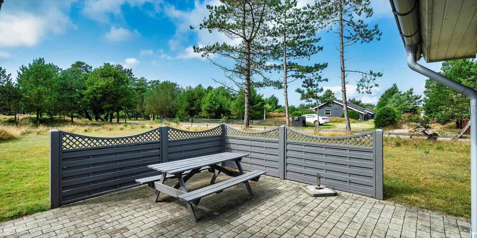 Terrasse mit Picknicktisch und Holzumrandung. Grünfläche und Bäume im Hintergrund.