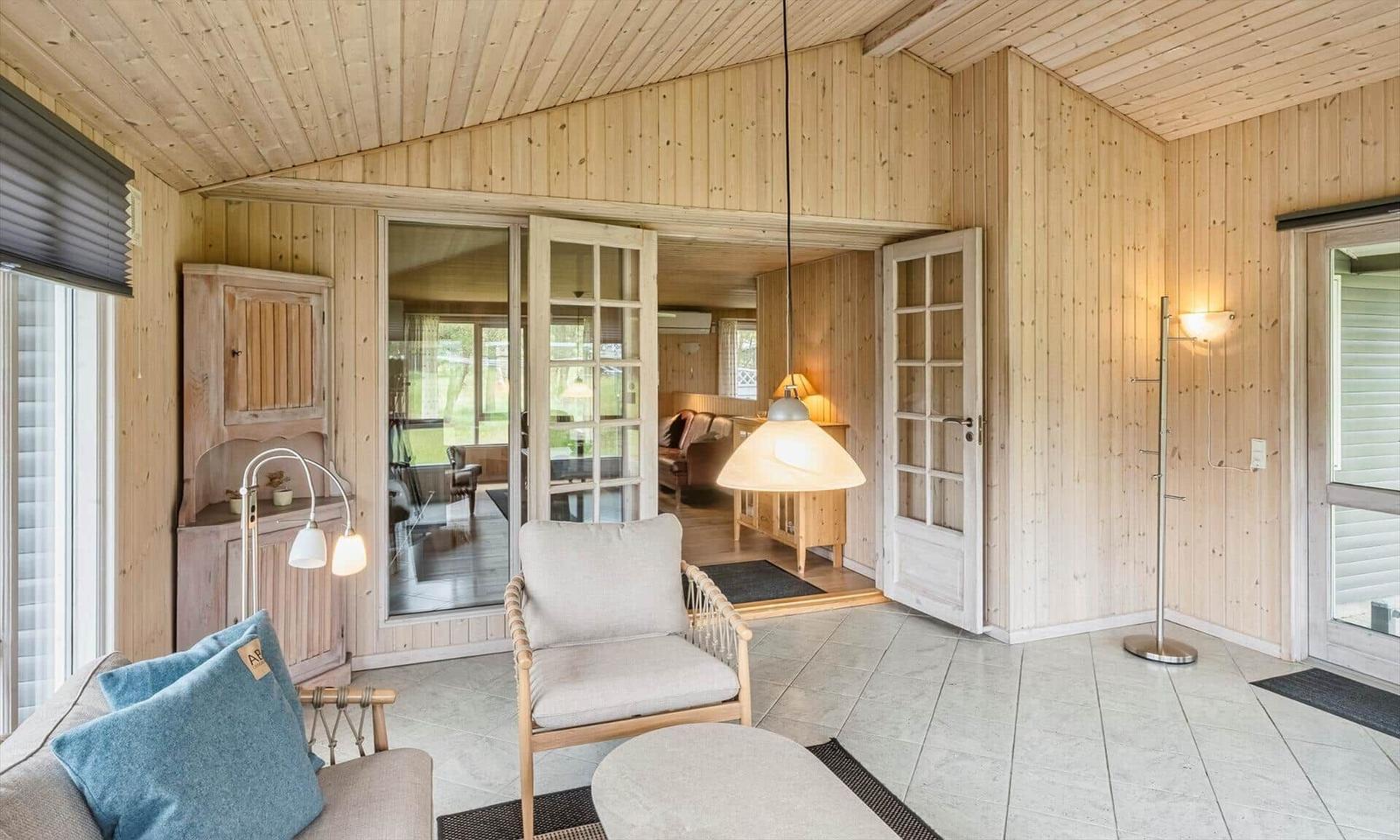 Wohnraum mit Holzwänden, Sitzmöbeln und Glas-Türen zum Garten.