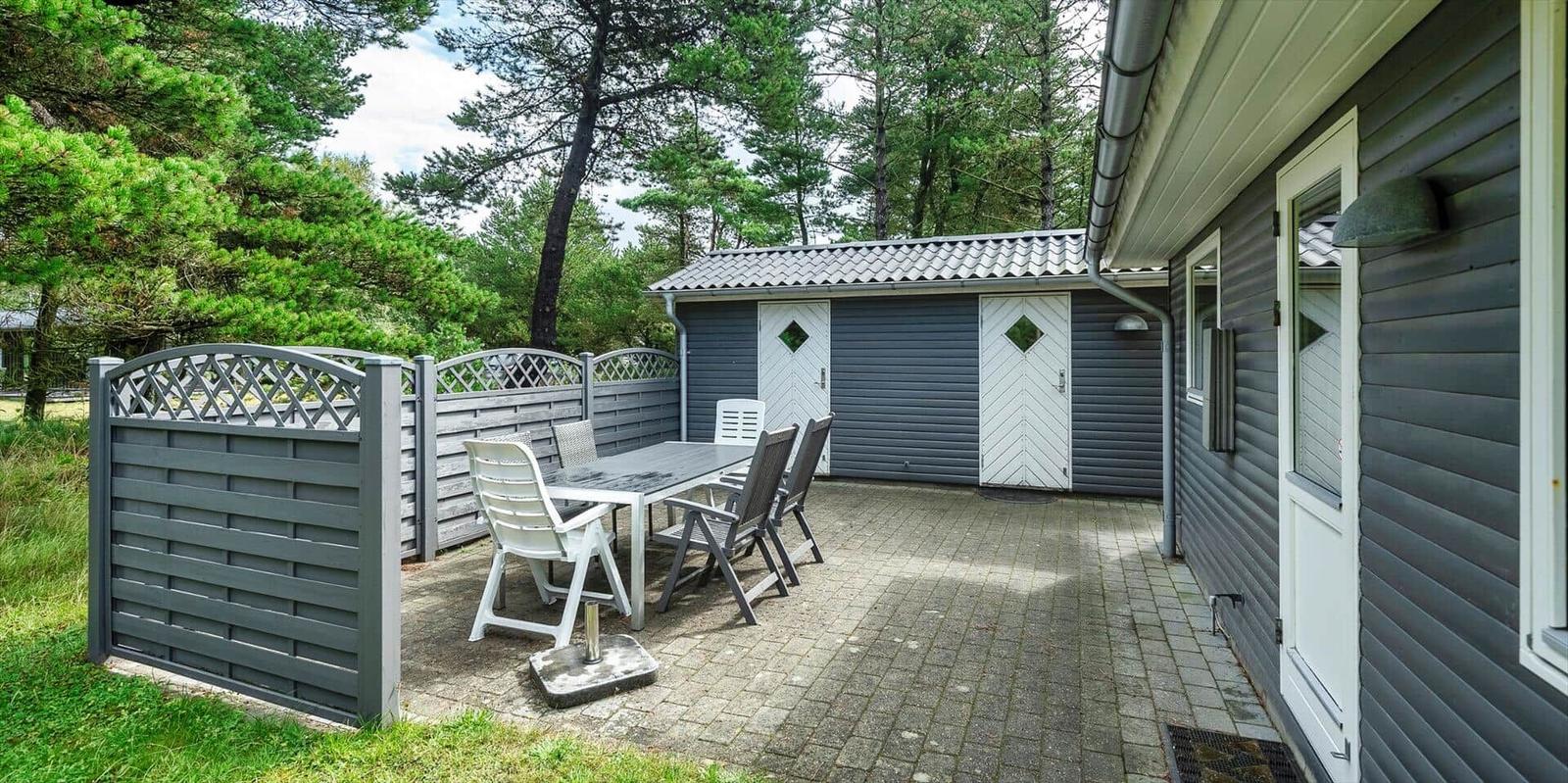 Terrasse mit Tisch und Stühlen neben einem grauen Gartenhaus.