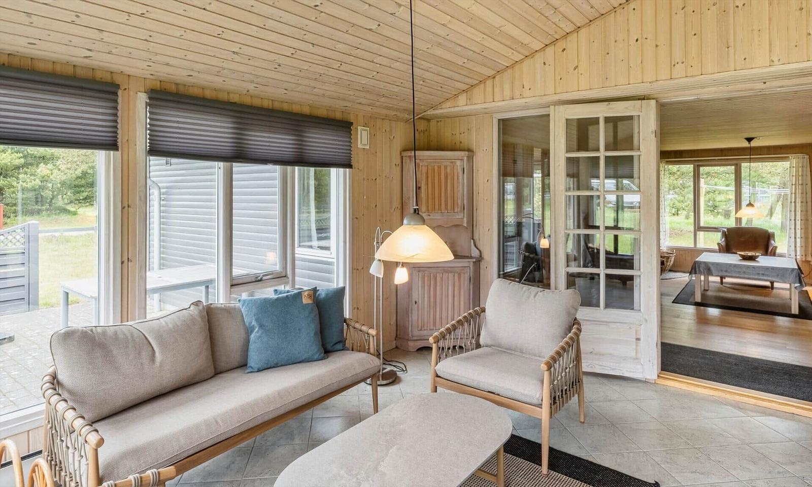 Wohnbereich mit Sofa, Sessel und Tisch. Holzwände und große Fenster.