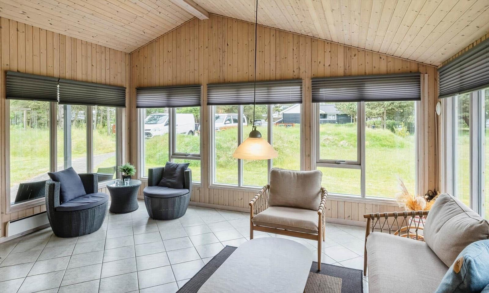 Wohnzimmer mit Holzwänden, großen Fenstern und Sitzgelegenheiten.