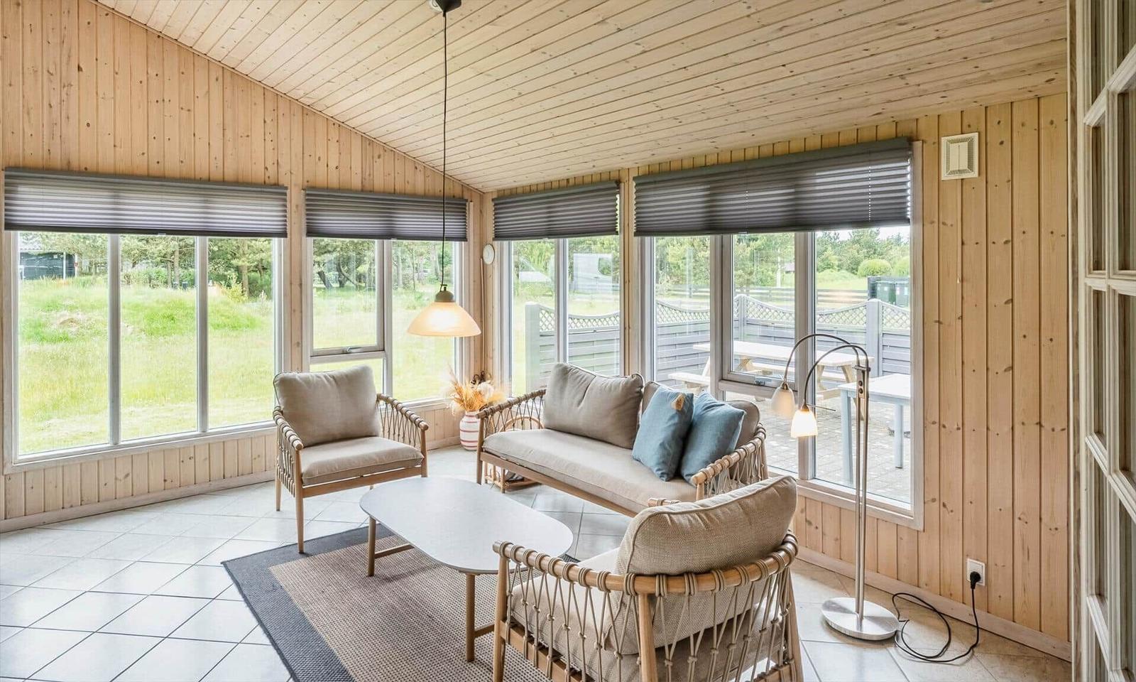 Wohnraum mit Holzwänden, Sitzgruppe und großen Fenstern zum Garten.