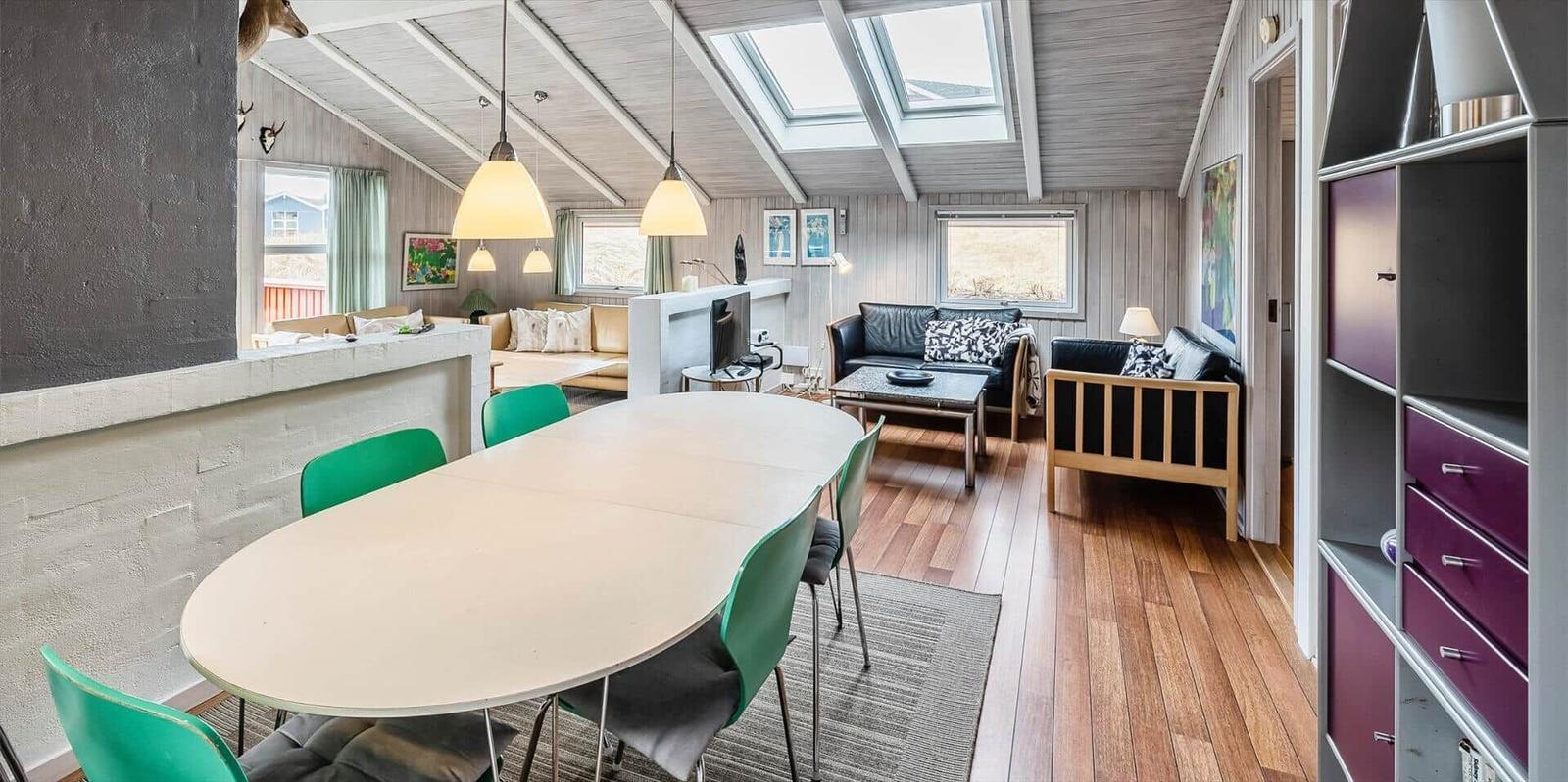 Essbereich mit Tisch und Stühlen, Wohnbereich mit Sofa und TV, Holzboden und Dachfenster.