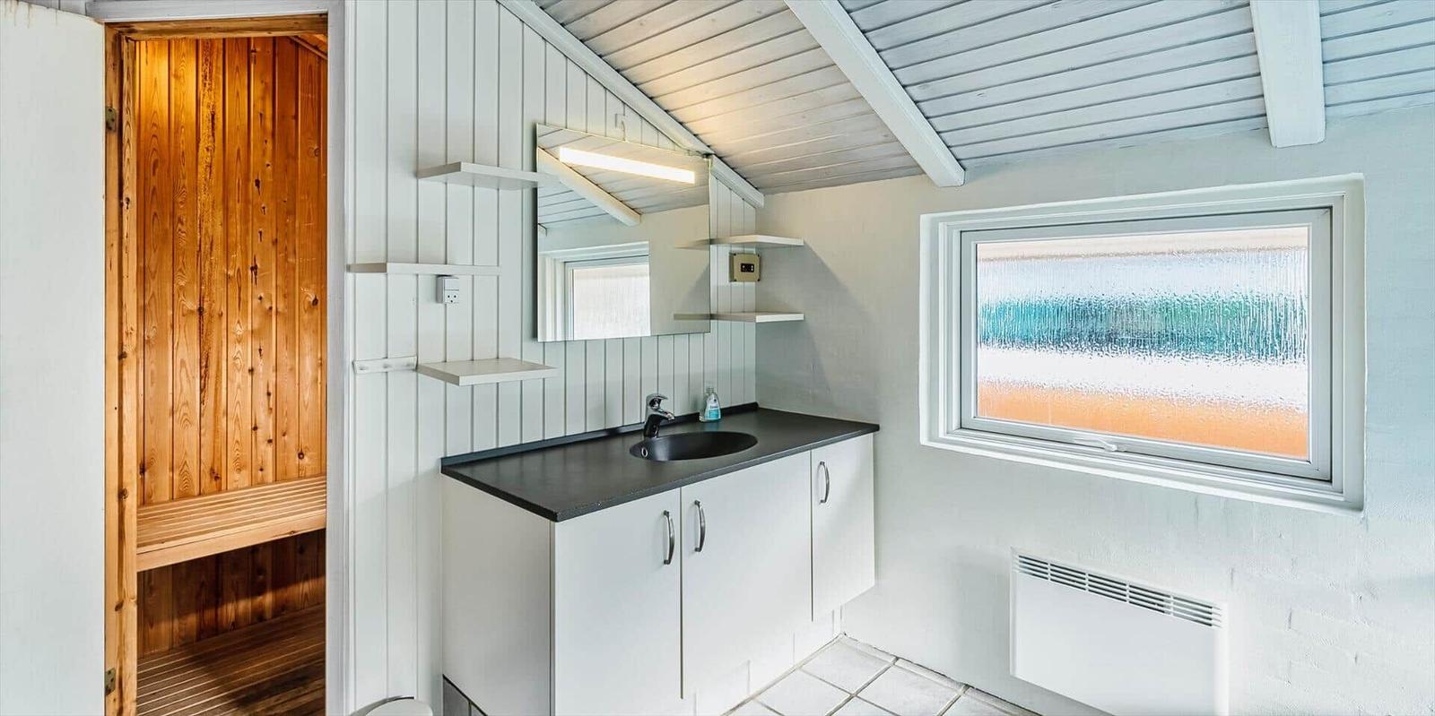 Badezimmer mit Waschbecken, Spiegel und Holzsauna