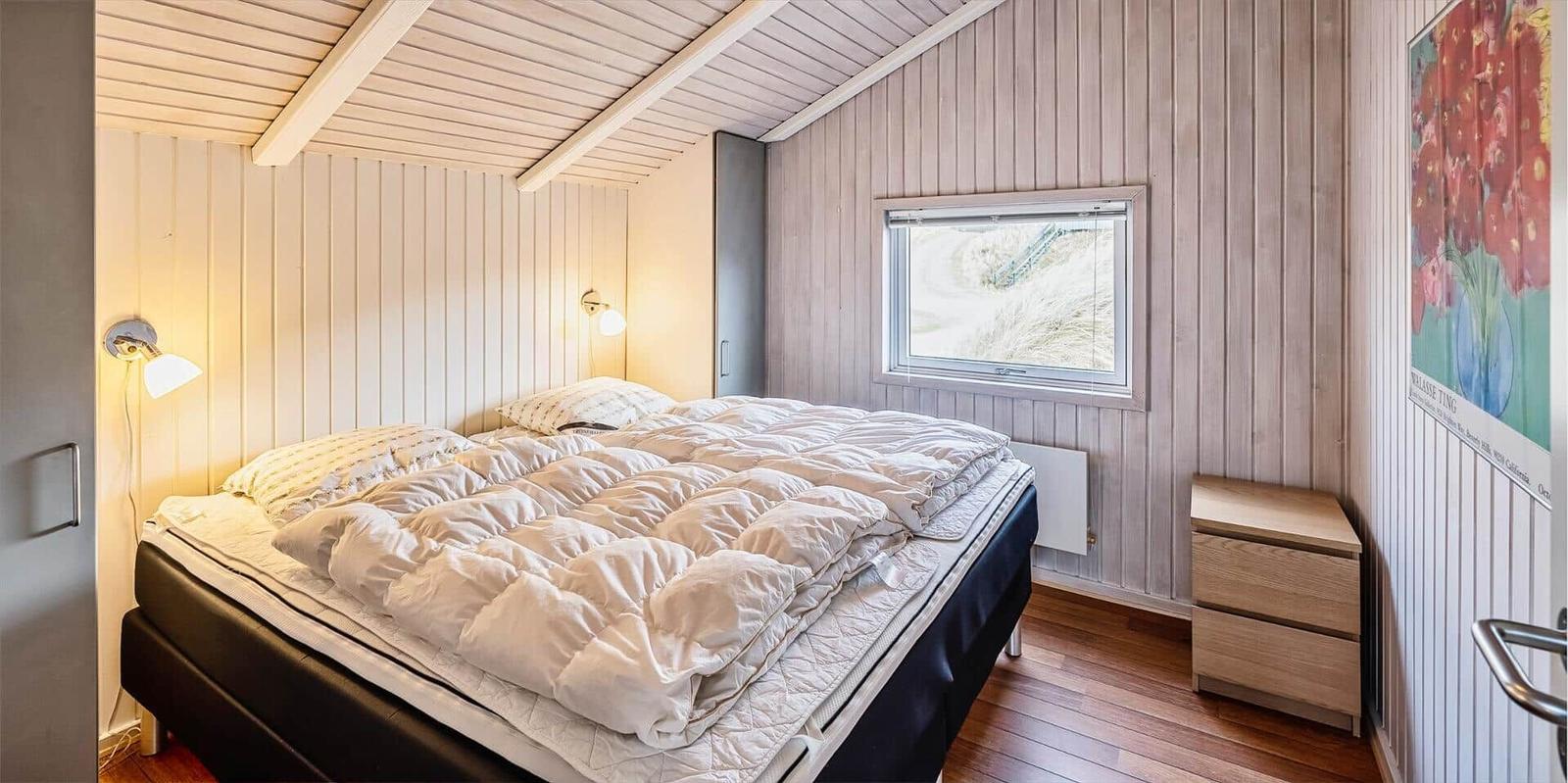 Schlafzimmer mit Bett, Nachttisch und Fenster. Holzwände und Decke.