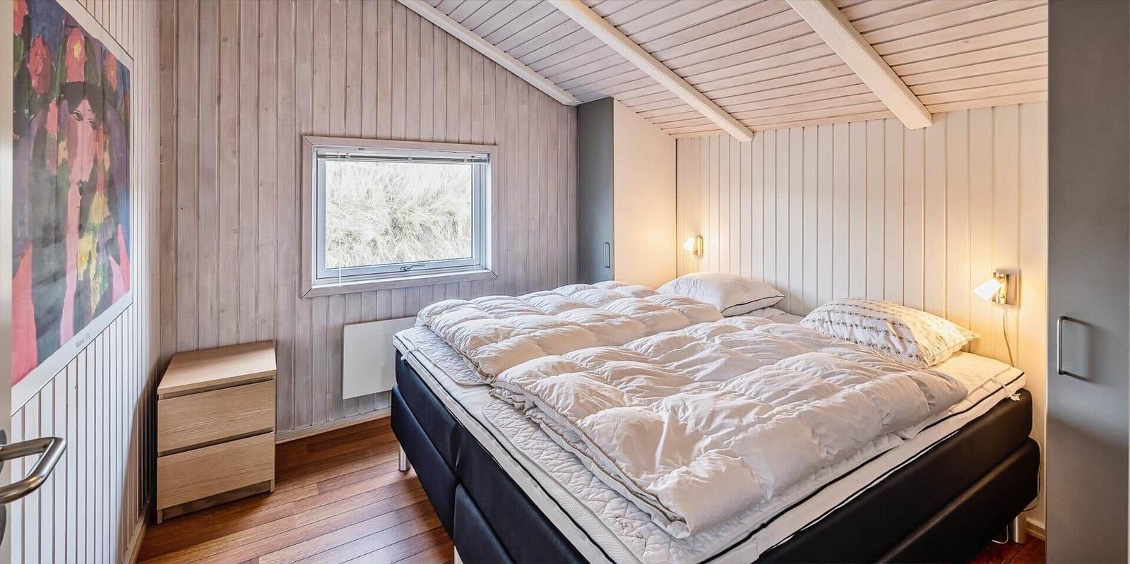 Schlafzimmer mit Bett, Fenster und Holzwandverkleidung.