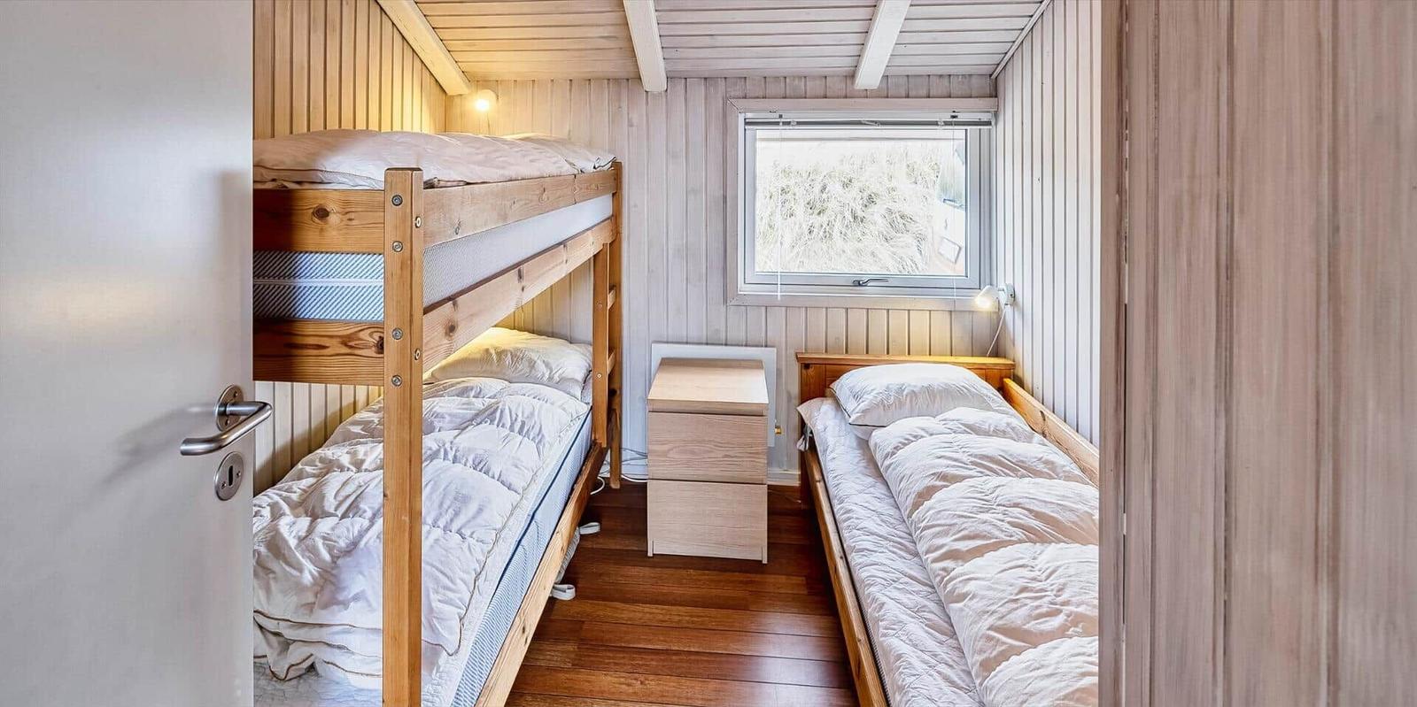 Zimmer mit Schlafcouch, Doppelbett und Fenster mit Blick auf Gras.