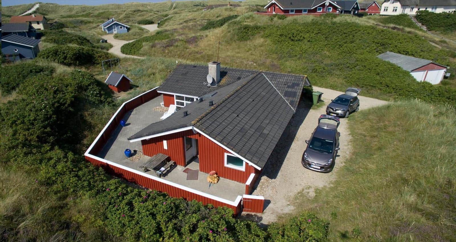Rotes Ferienhaus mit Garage und Terrasse auf grüner Hügellandschaft.