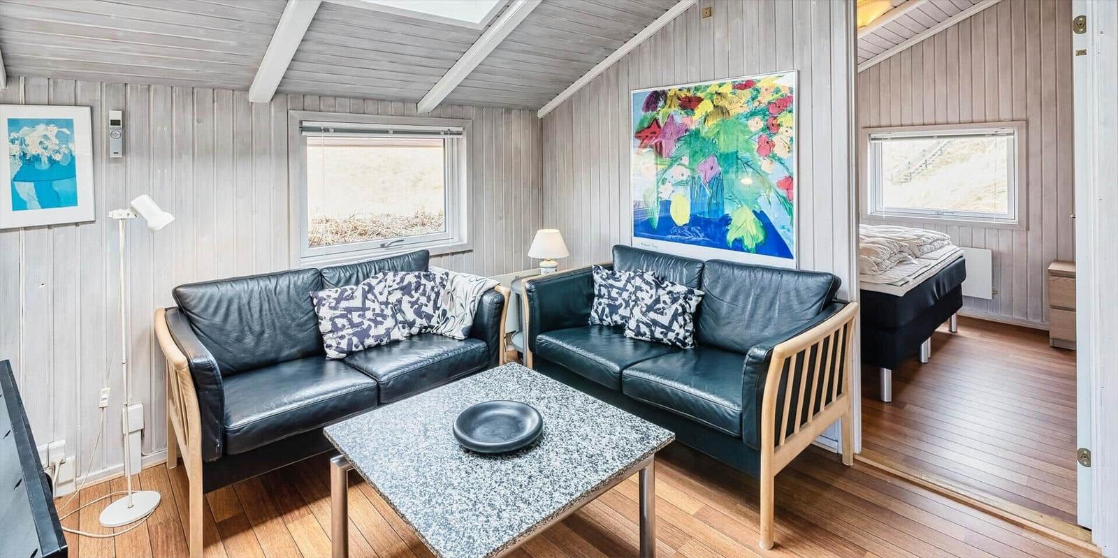 Wohnzimmer mit zwei Ledersofas, Tisch und Wandbild. Blick in Schlafzimmer mit Bett.