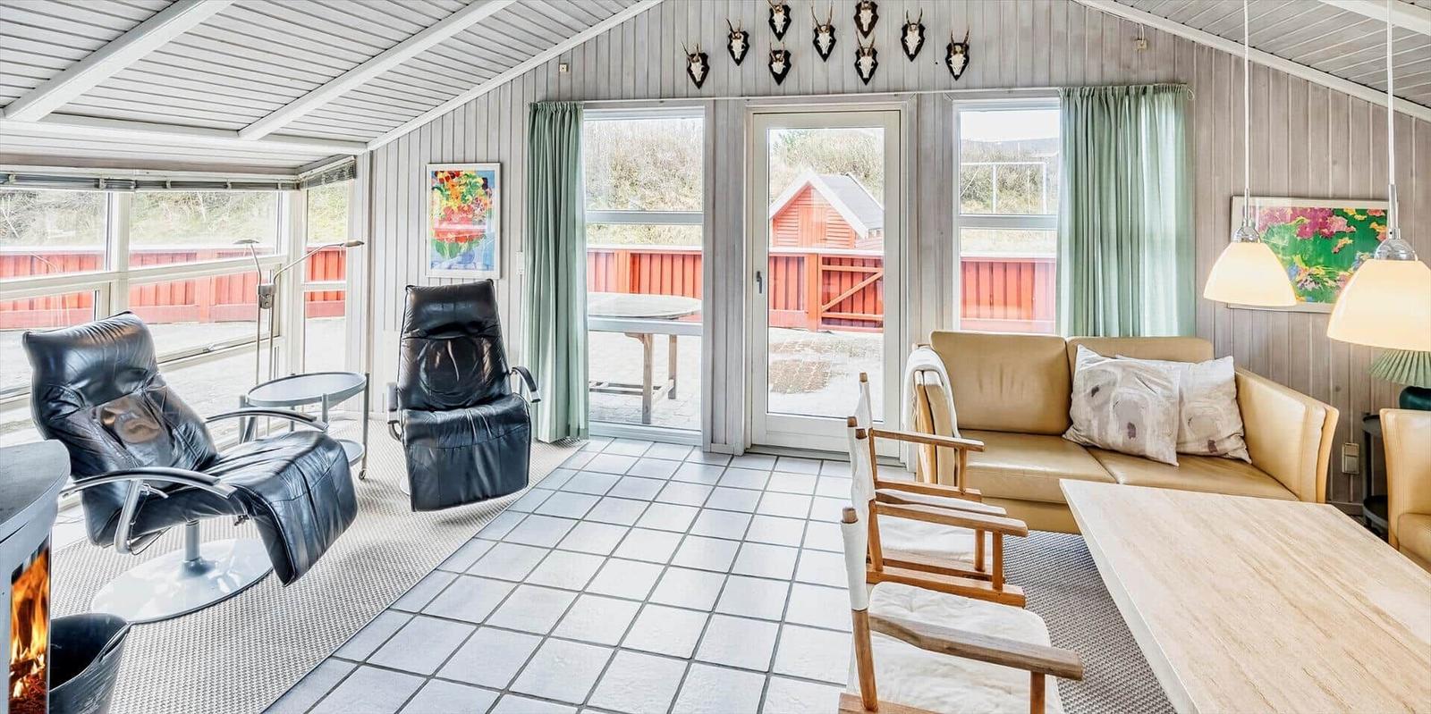 Wohnraum mit Sofa, Sessel und Kamin. Große Fenster und Tür zur Terrasse.