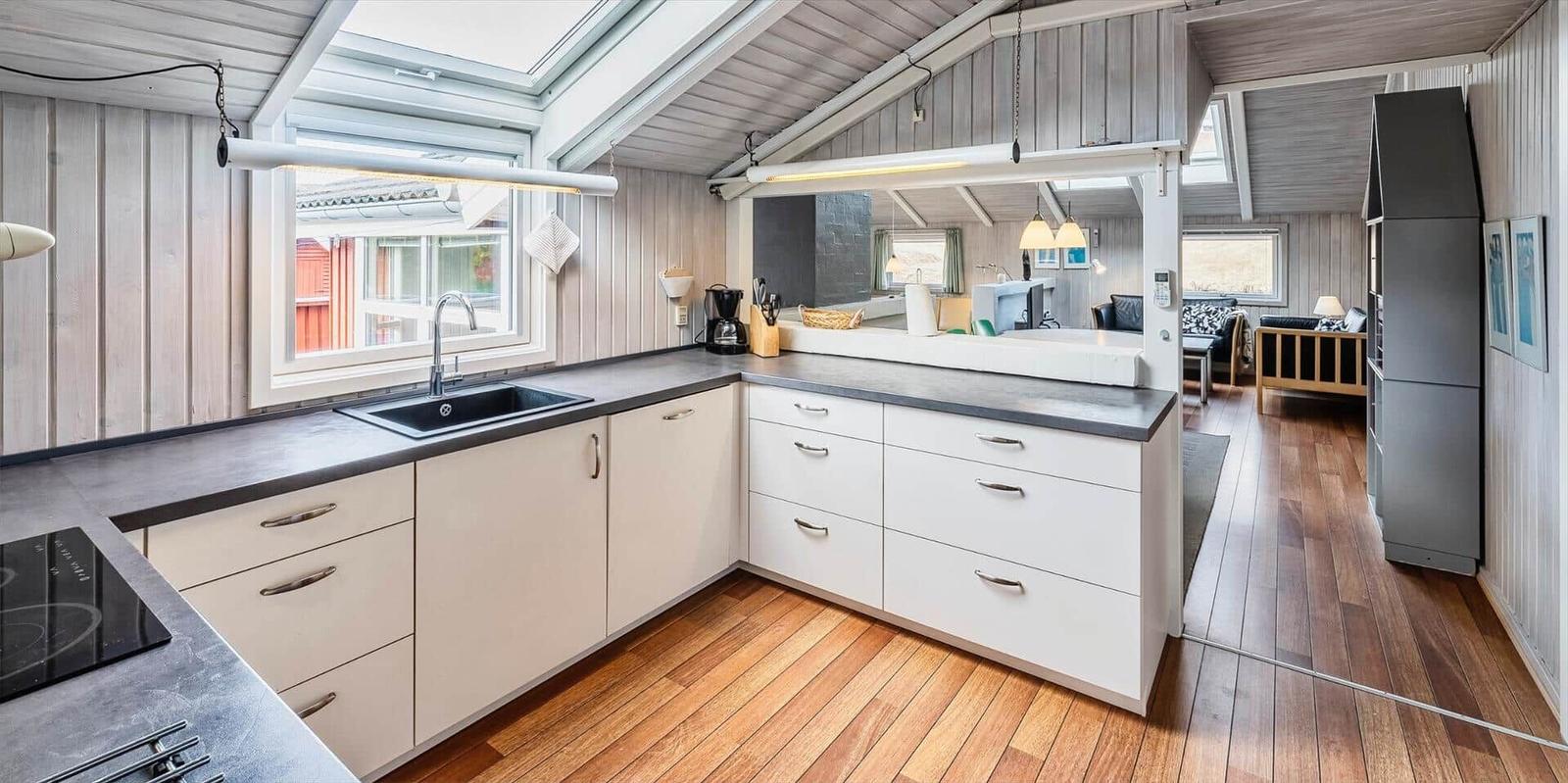 Küche mit Arbeitsfläche, Spüle und Fenster. Blick in Wohnbereich mit Sofa und Kühlschrank.