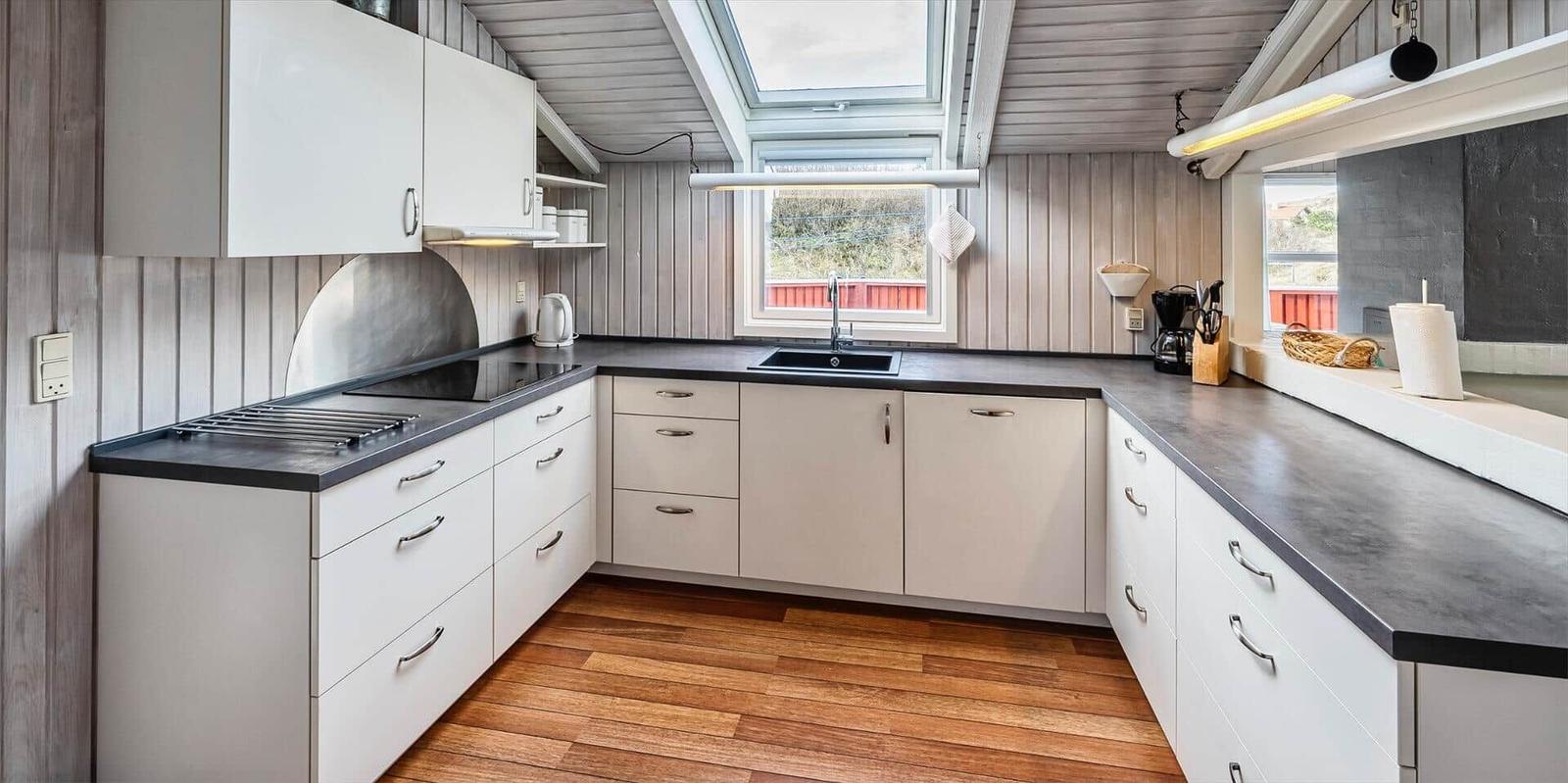 Küche mit weißen Schränken, dunklem Arbeitsplatz und Holzboden unter Dachschrägen.