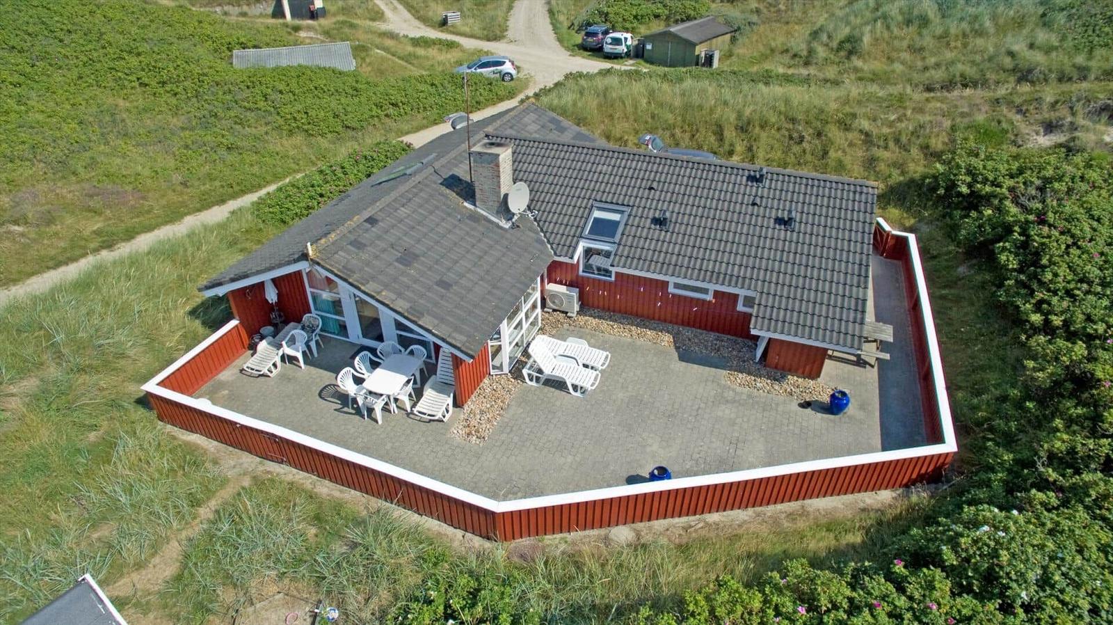 Rotes Ferienhaus mit Terrasse und Garten, umgeben von Gras und Bäumen.