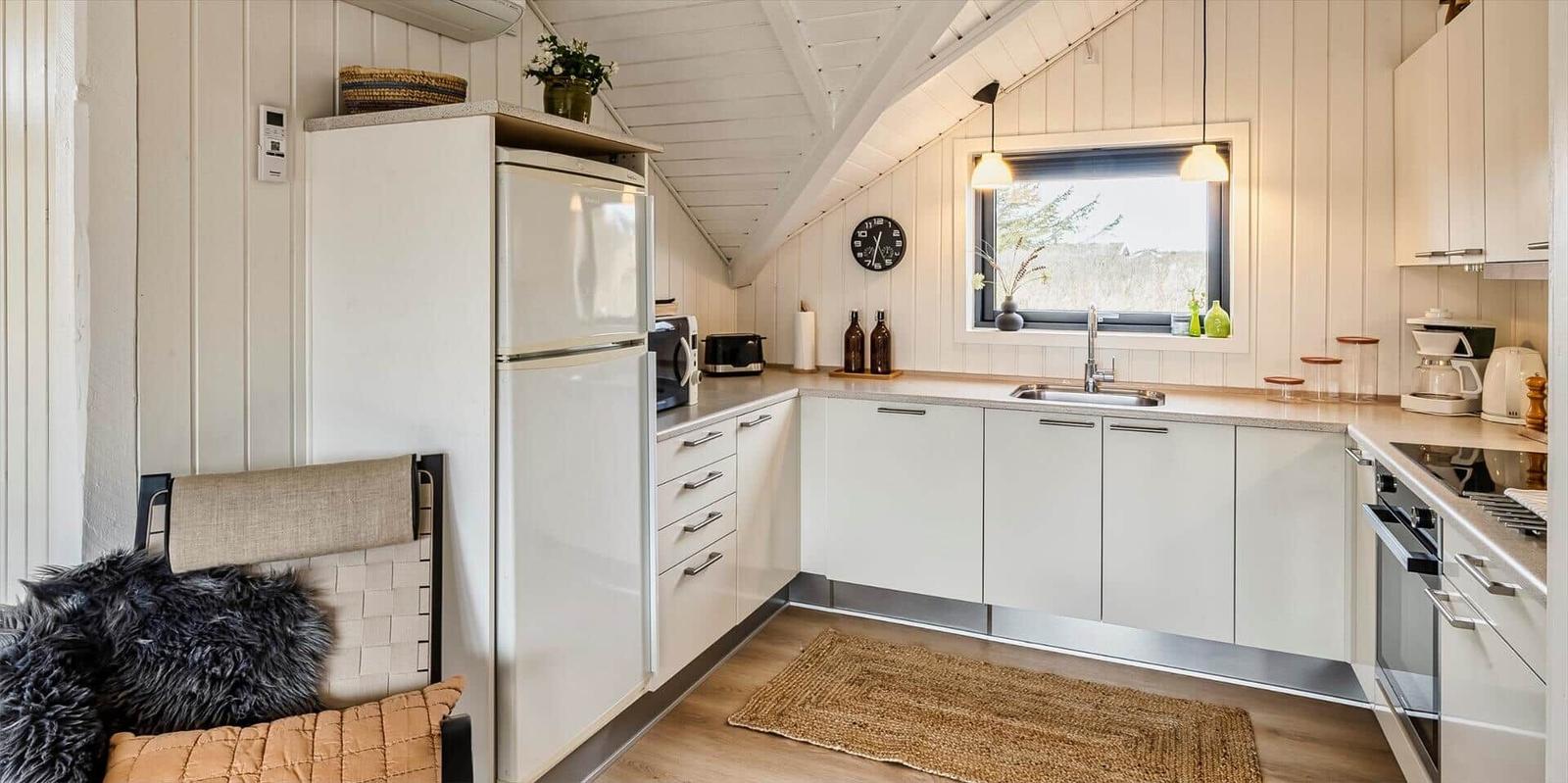 Küche mit weißem Schrank, Kühlschrank, Spüle und Fenster. Holzfußboden und Deckenbalken.