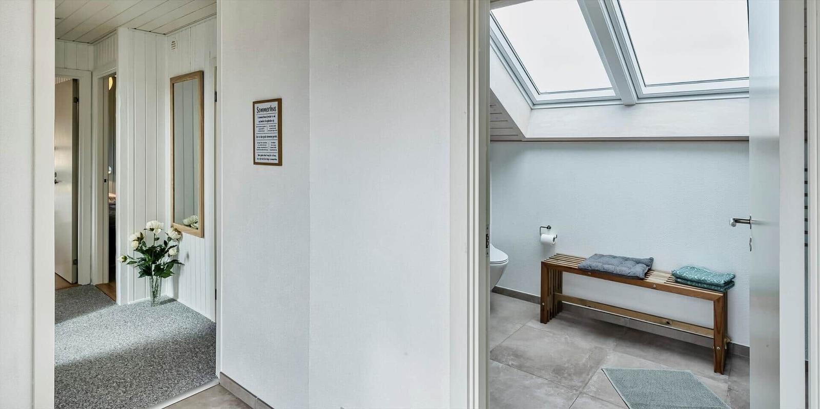 Badezimmer mit Dachfenster und Holzbank. Flur mit Spiegel und Blumen.