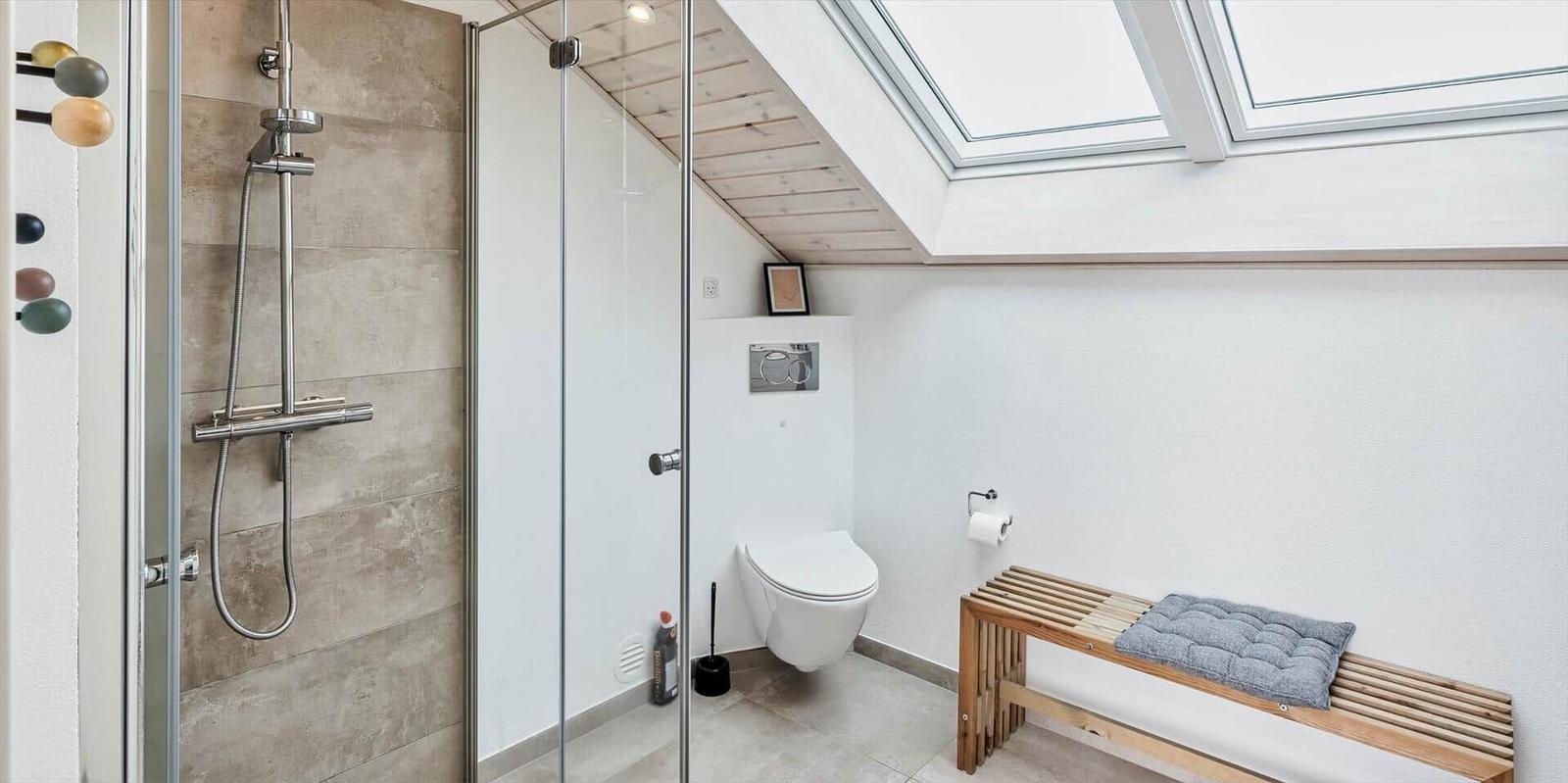 Dusche mit Glaswand, Toilette und Holzbank unter Dachschrägen mit Dachfenstern.