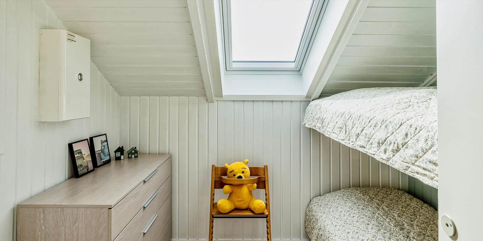 Kinderzimmer mit Doppelstockbett, Stuhl und Schrank unter Dachschräge mit Dachfenster.