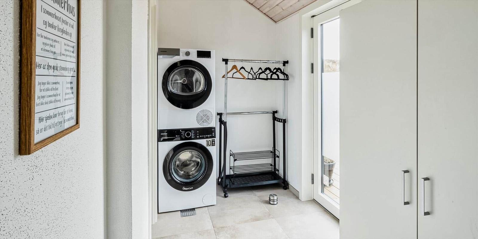 Waschmaschine und Trockner in einem Raum mit Garderobe und Tür zum Balkon.