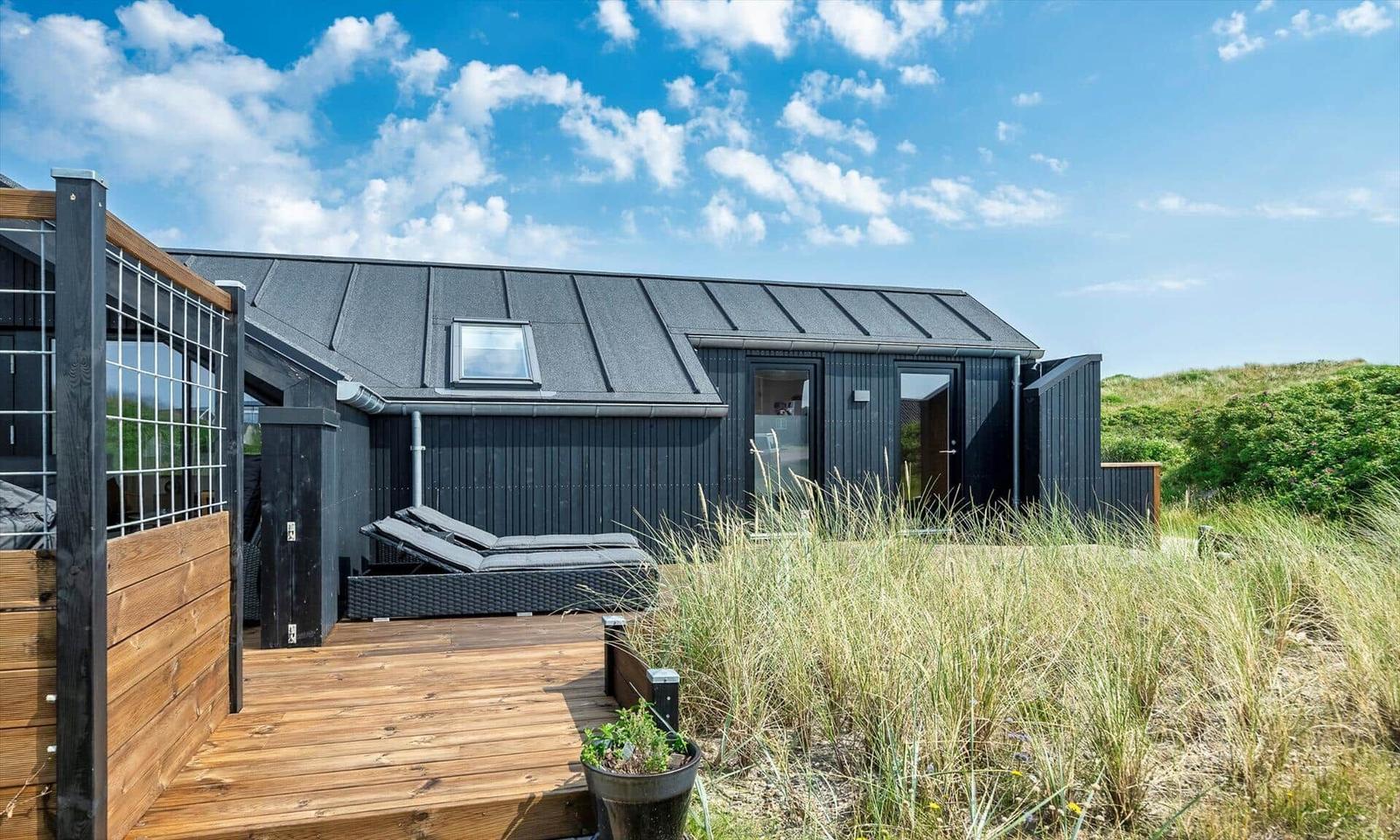 Schwarzes Haus mit Terrasse und Liegen im Gras