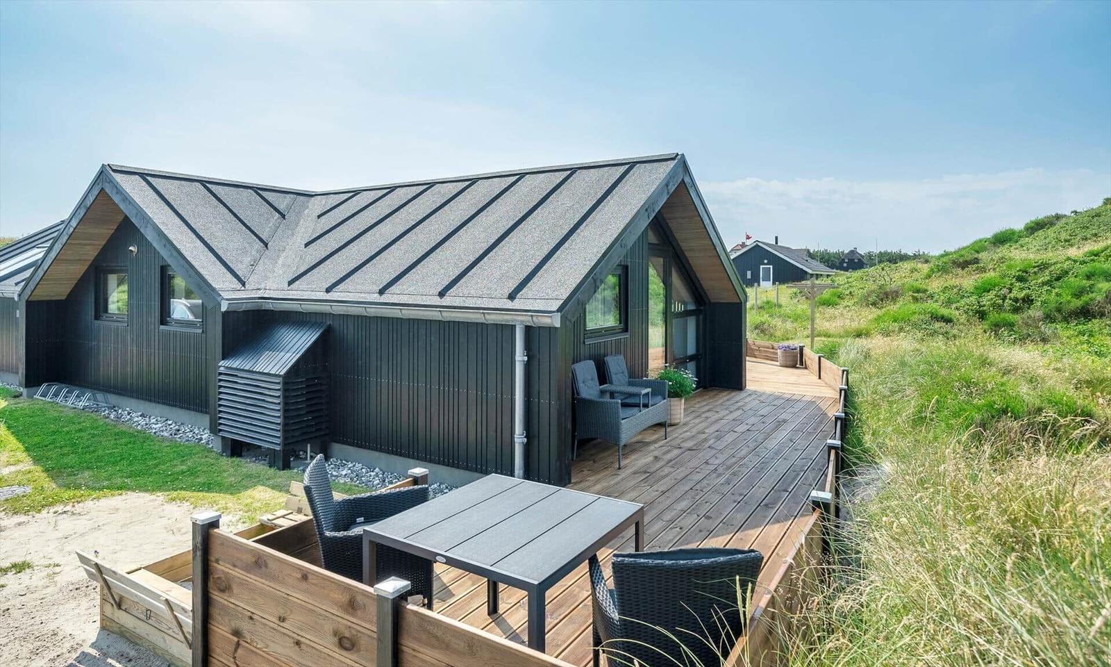 Moderne Strandhütte mit Holzterrasse und Gartenmöbeln.