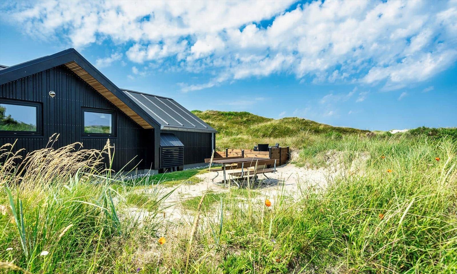 Moderne Holzhütte mit Außentisch in Grasland unter blauem Himmel.