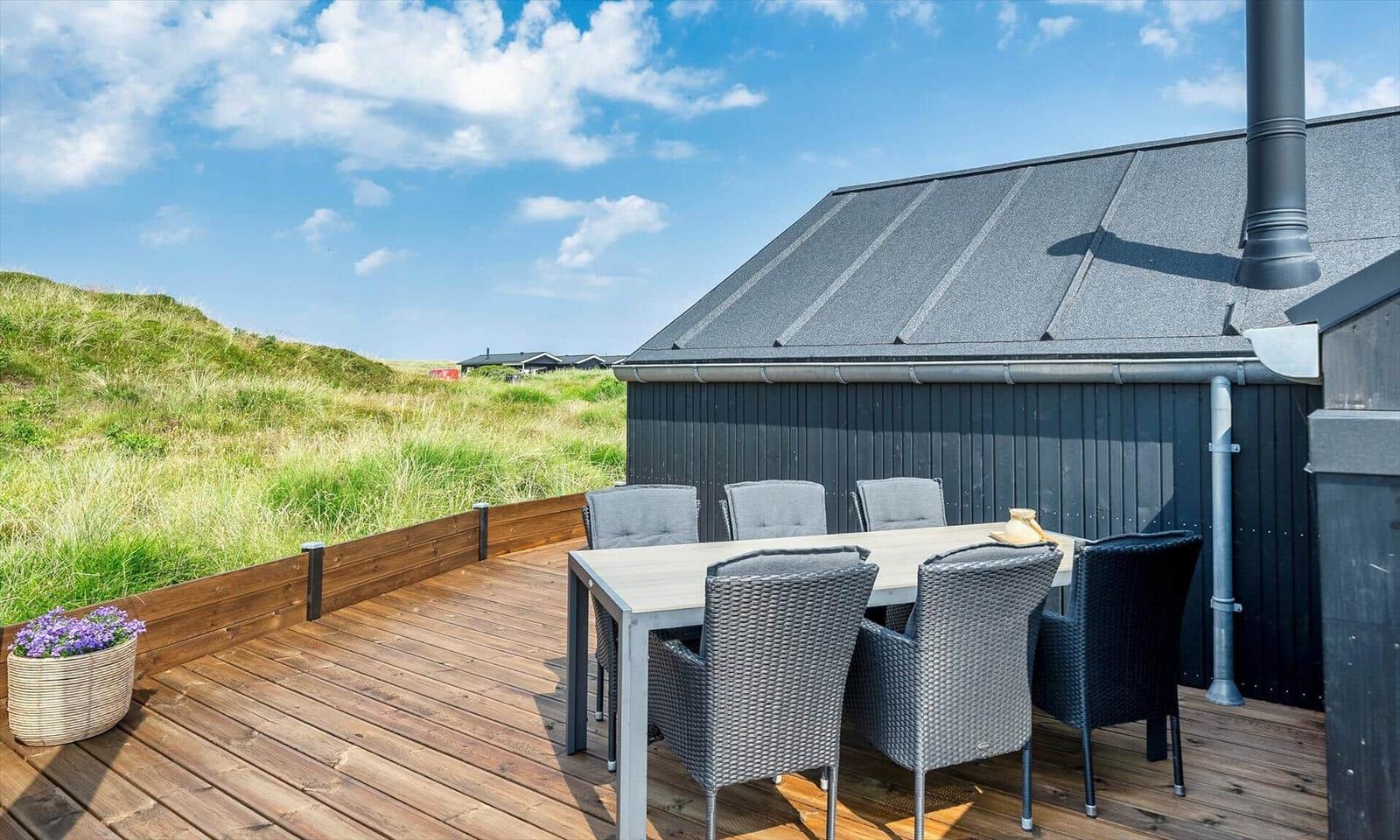 Terrasse mit Tisch und Stühlen neben einem Haus mit grauem Dach.
