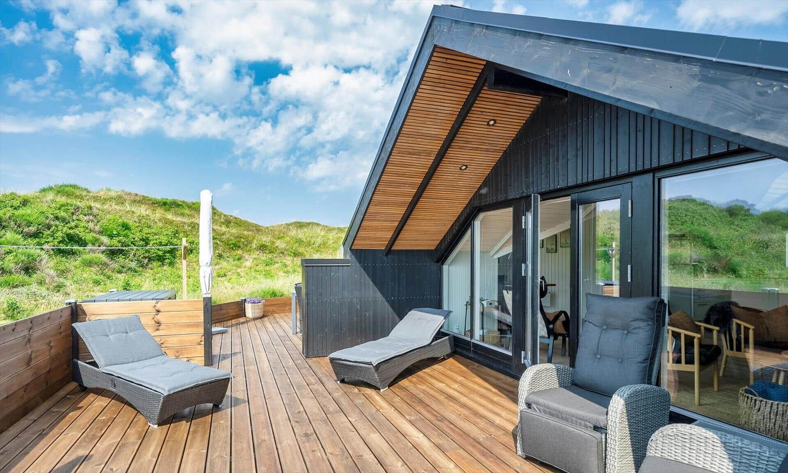 Terrasse mit Liegen und Sitzgelegenheiten vor modernem Haus mit Holzverkleidung und Glasfront.