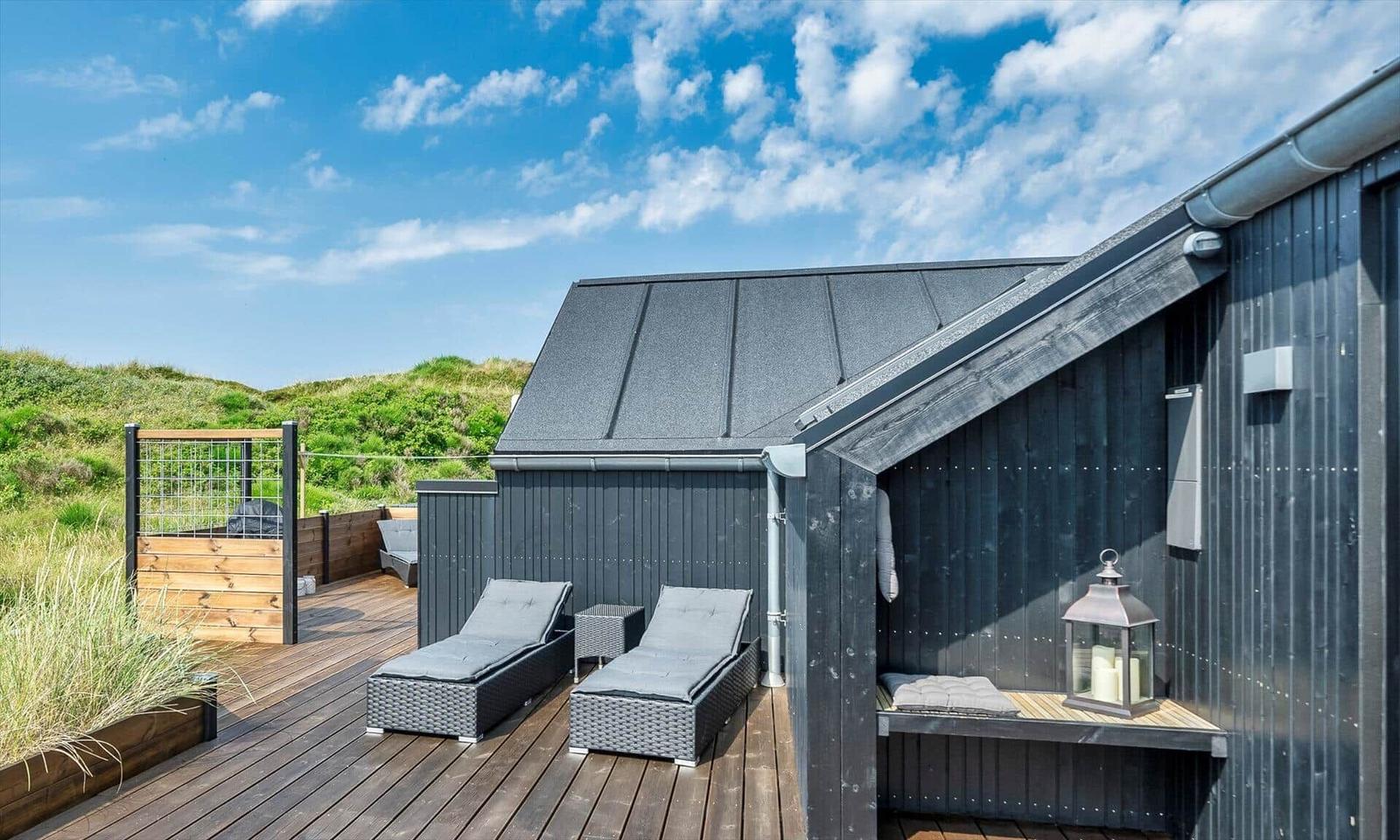 Terrasse mit Liegen und Sitzbank neben einem dunklen Holzhaus.