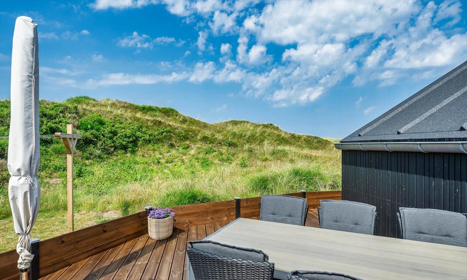 Terrasse mit Tisch, Stühlen und Blick auf grüne Dünen.