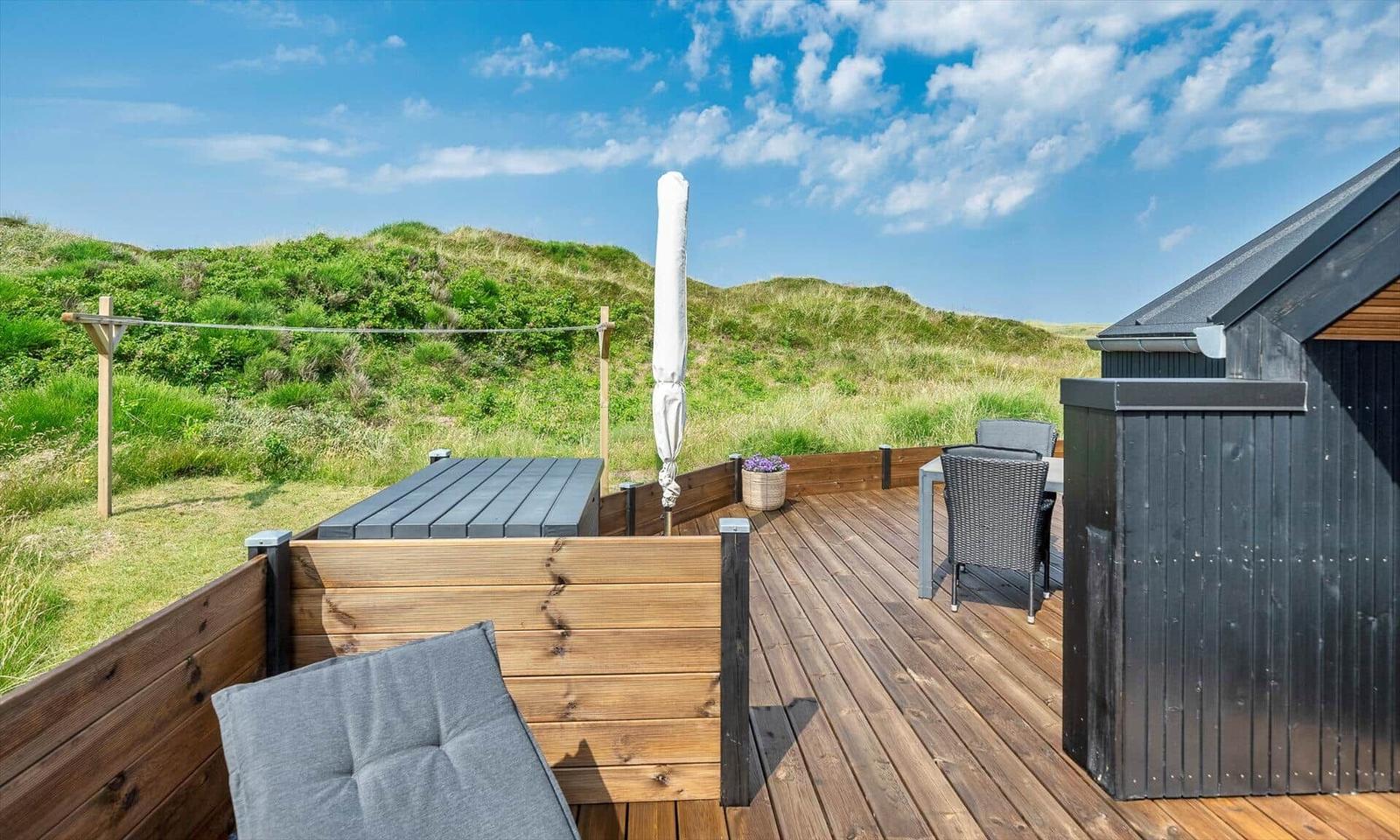 Terrasse mit Tisch, Stühlen und Blick auf grüne Dünen.