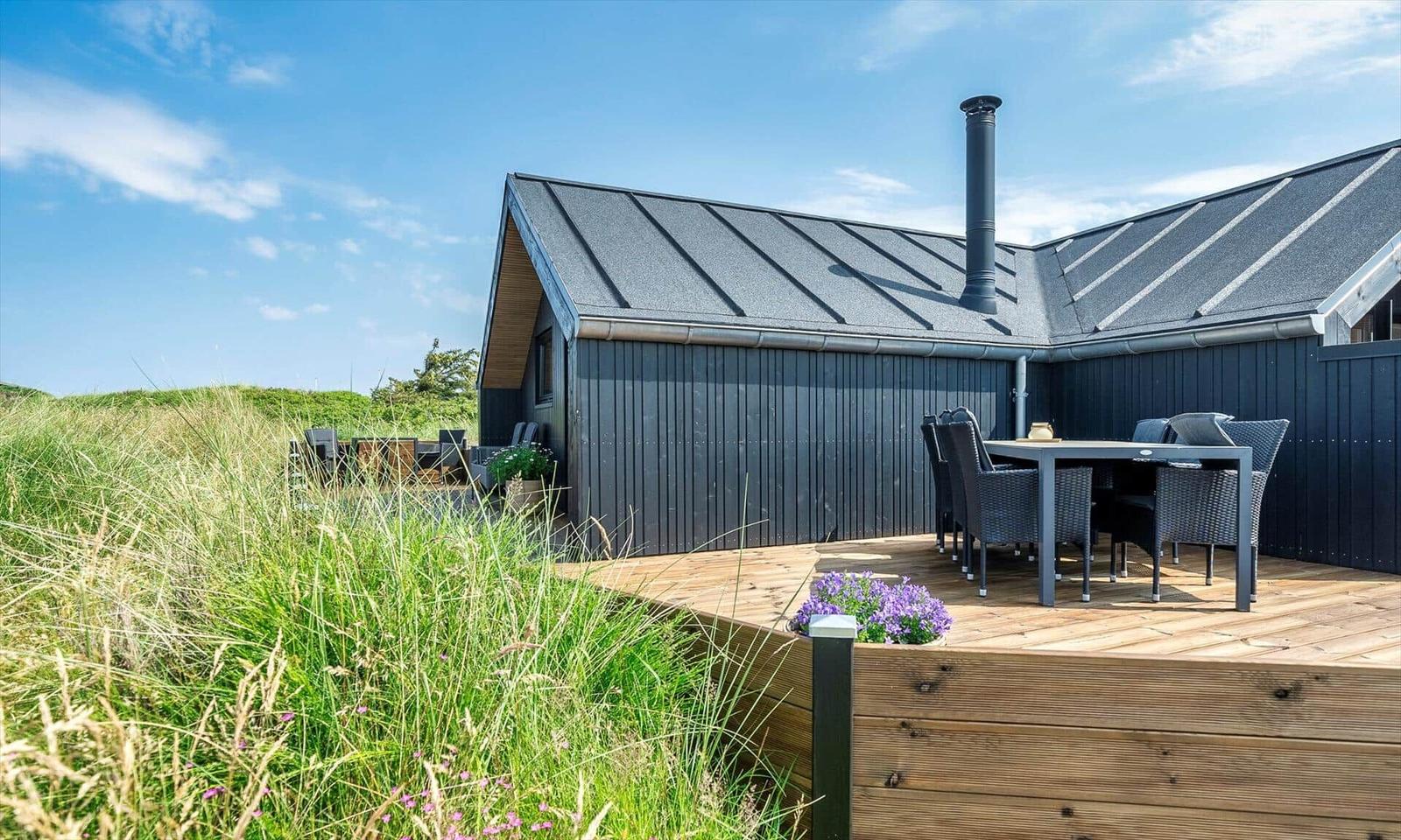 Moderne Hütte mit Holzterrasse, Gartenmöbeln und Grillmöglichkeit im Freien.