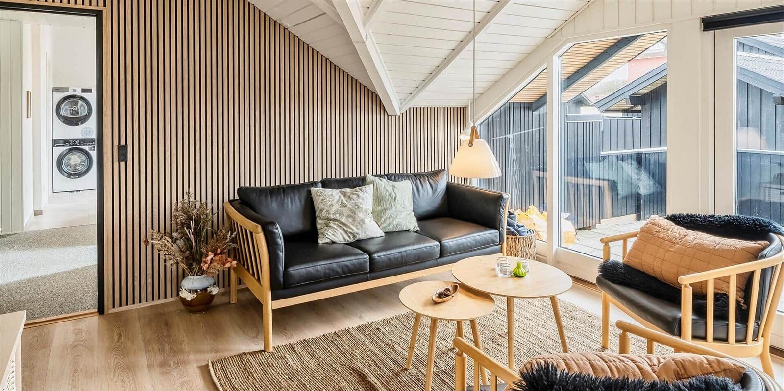 Wohnzimmer mit Sofa, Sessel und Tischen. Durchgang zu Waschmaschine und Trockner.