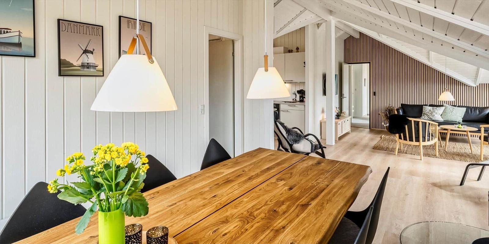 Essbereich mit Holztisch und schwarzen Stühlen. Im Hintergrund Wohnzimmer und Küche.