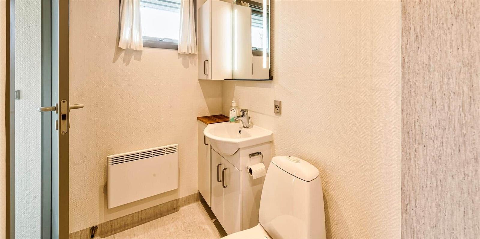 Badezimmer mit Waschbecken, Spiegelschrank und Toilette. Fenster mit Vorhängen und Heizkörper.