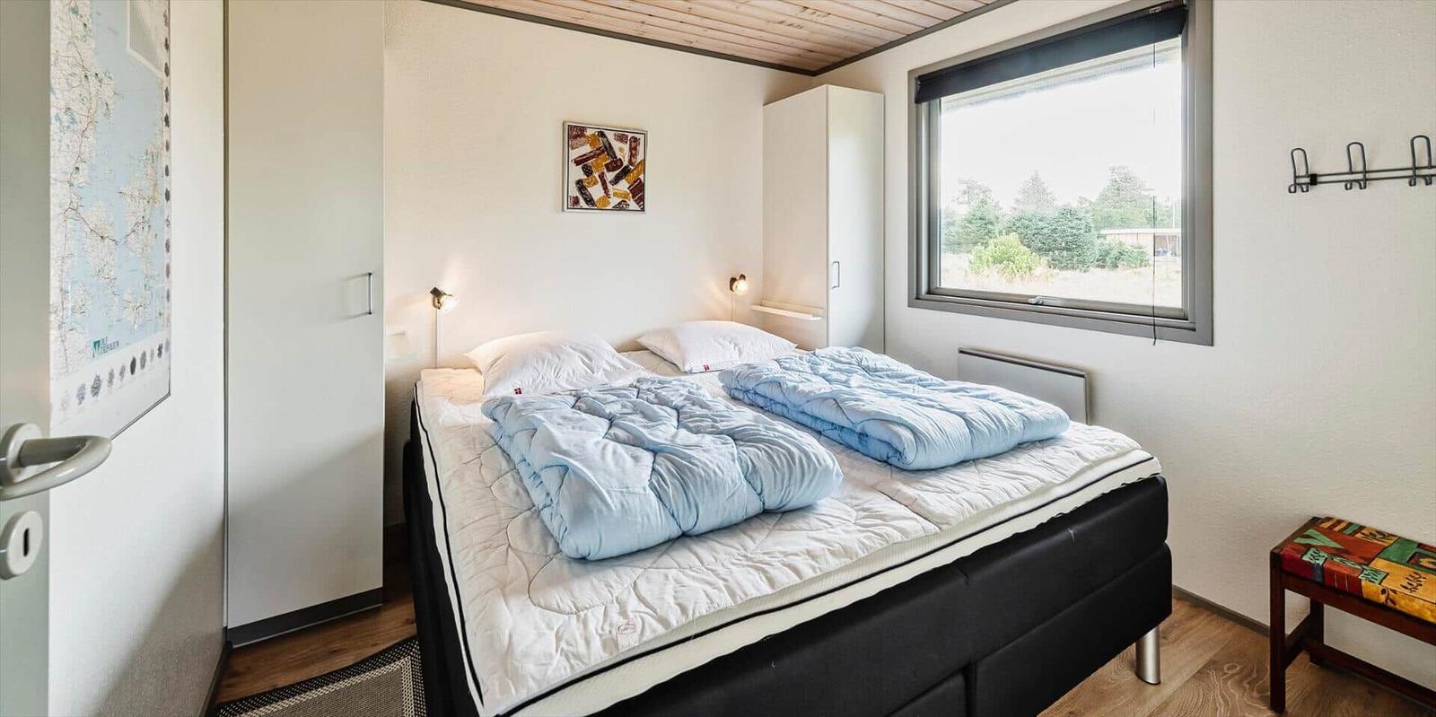 Schlafzimmer mit Doppelbett, Fenster und Kleiderhaken an der Wand.